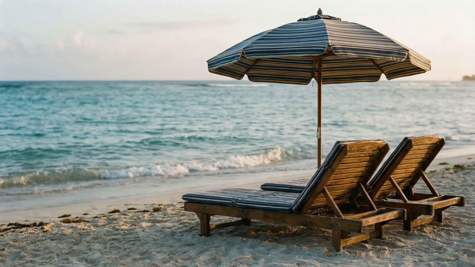 Quiet Morning Chairs 壁紙 — 兩張帶藍色坐墊的木製沙灘椅放在條紋遮陽傘下的沙灘上，溫柔的海浪拍打著岸邊。