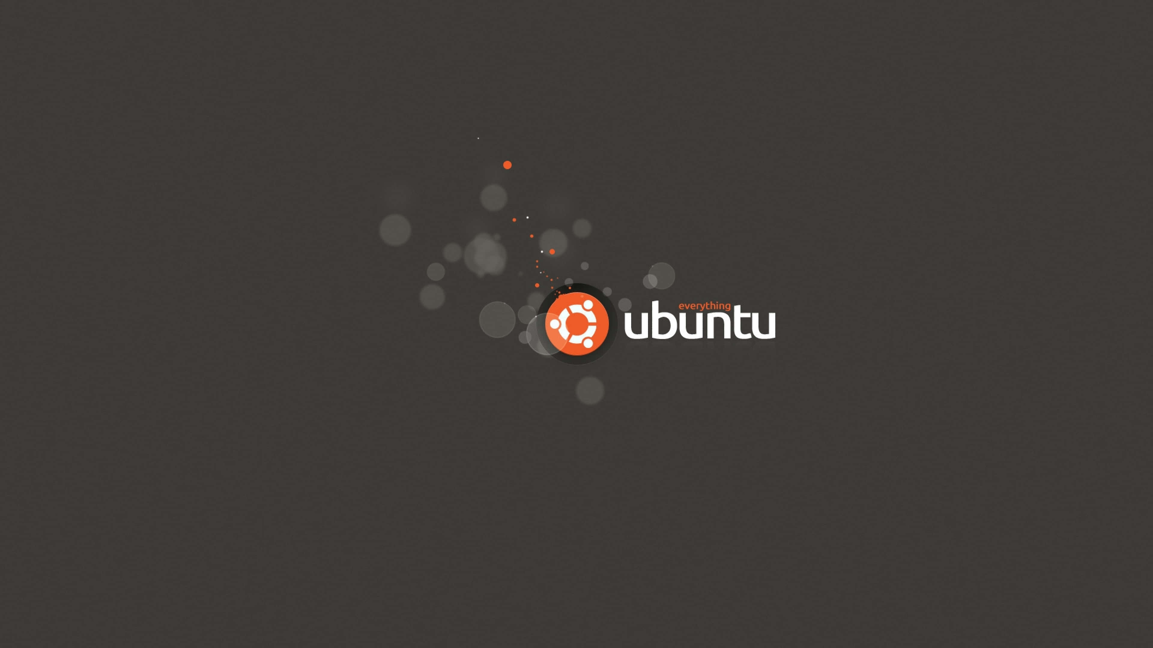 Ubuntu 4K 桌布 壁紙 — Ubuntu 標誌，橙色圓圈和白色文字居中在深灰色背景上，帶有微弱的發光粒子。