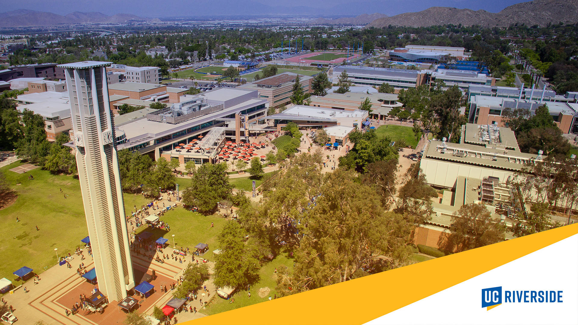  壁紙 — UC Riverside 校園的鳥瞰圖，標誌性塔樓、綠色草坪和學生在晴朗天空下聚集。