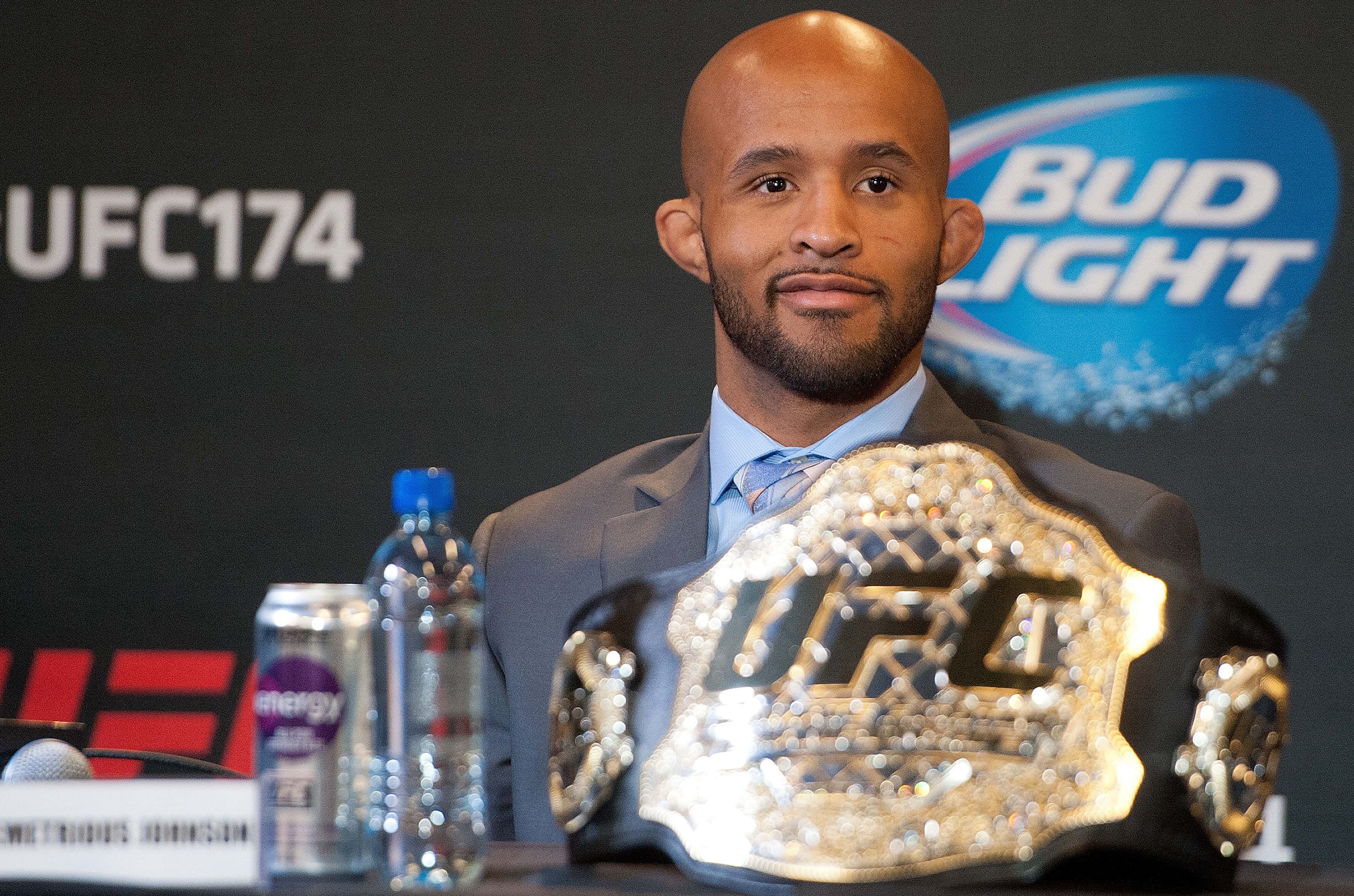 UFC 桌布 壁紙 — UFC拳手喬恩·瓊斯自信地坐在新聞發布會上，手持冠軍腰帶，表情嚴肅。