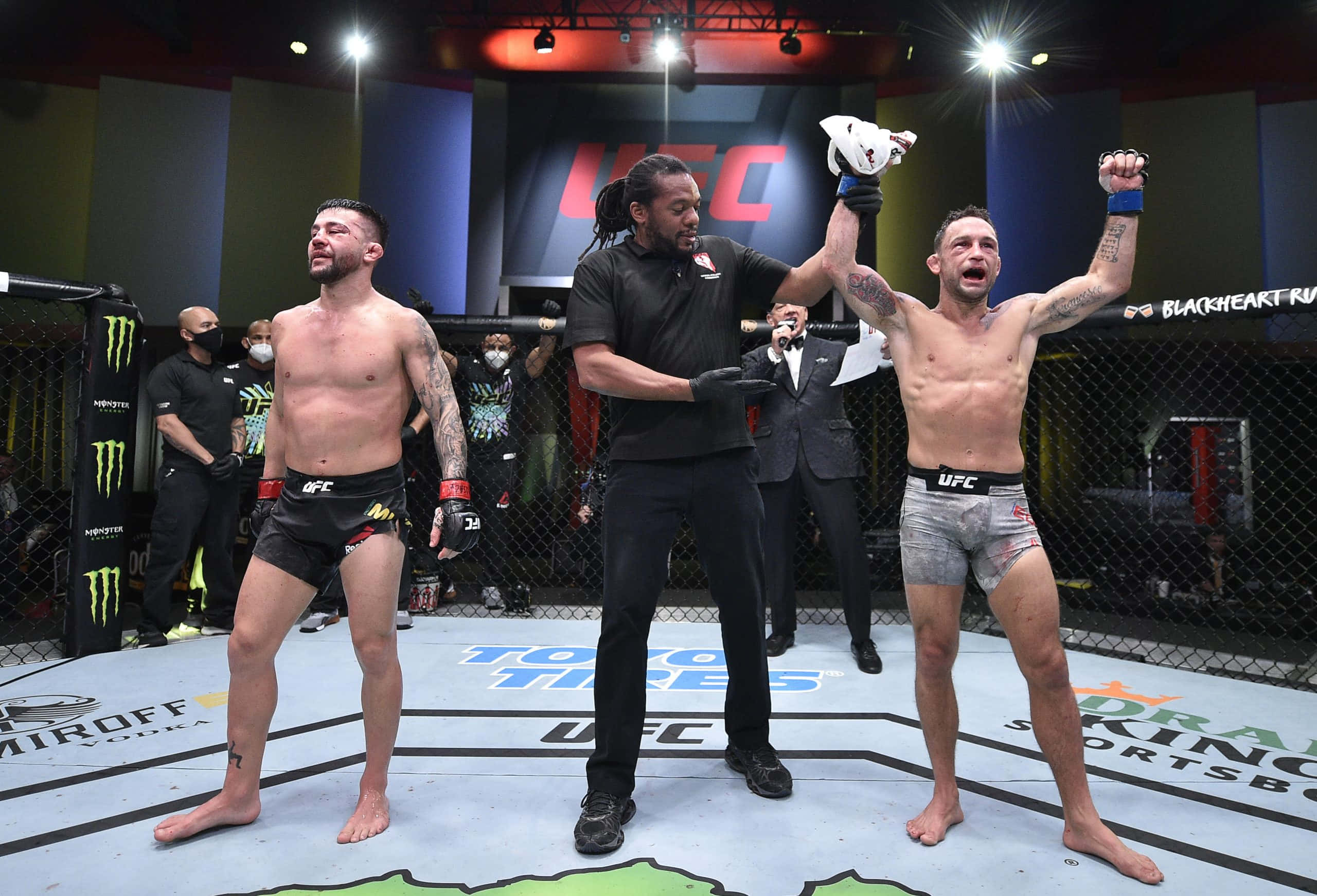 UFC 桌布 壁紙 — UFC拳手慶祝勝利，裁判在八角籠中舉起他的手，對手沮喪地站在附近。