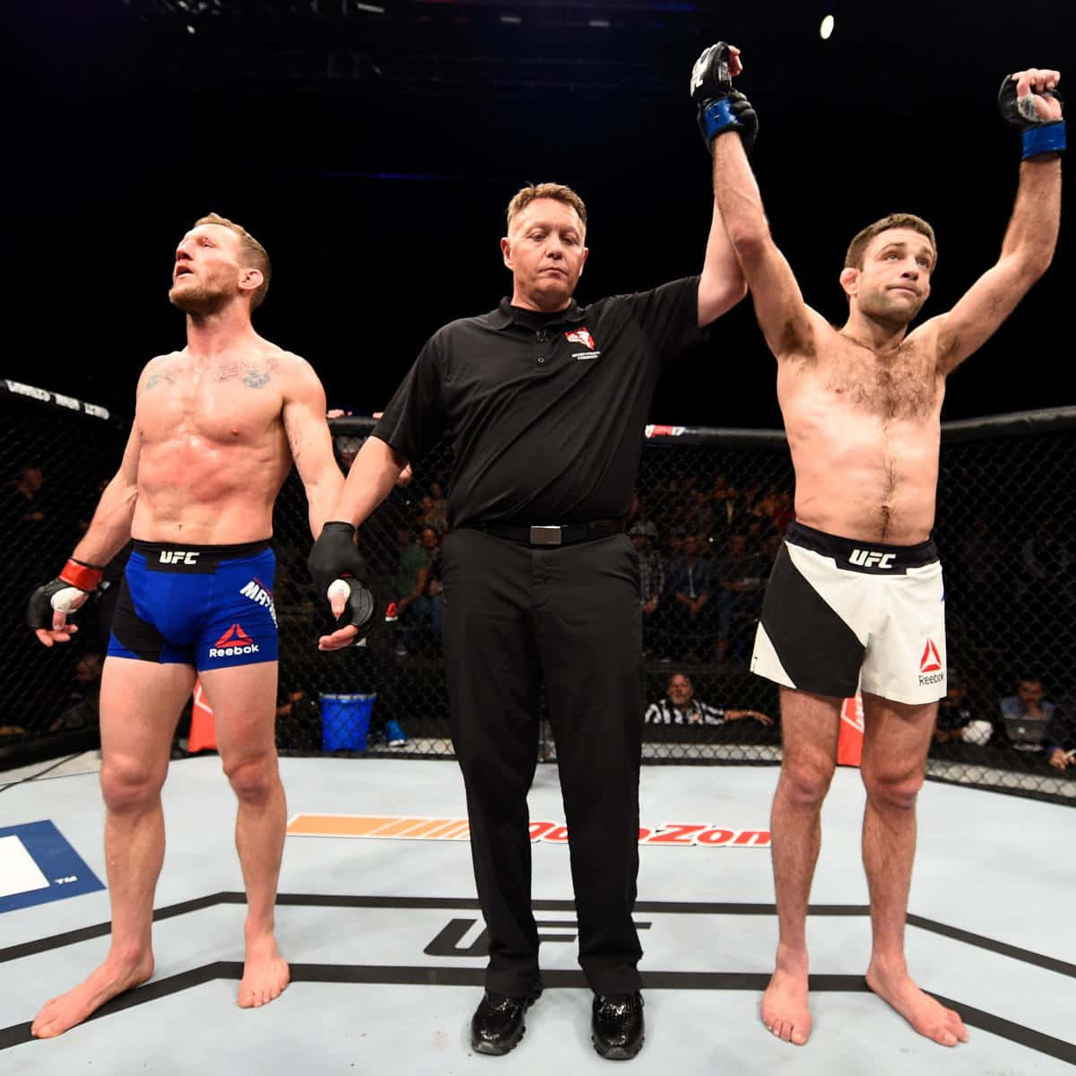 Fight 桌布 壁紙 — UFC裁判在八角籠中舉起勝利的拳手的手臂，而對手在場館燈光下敗北站立。