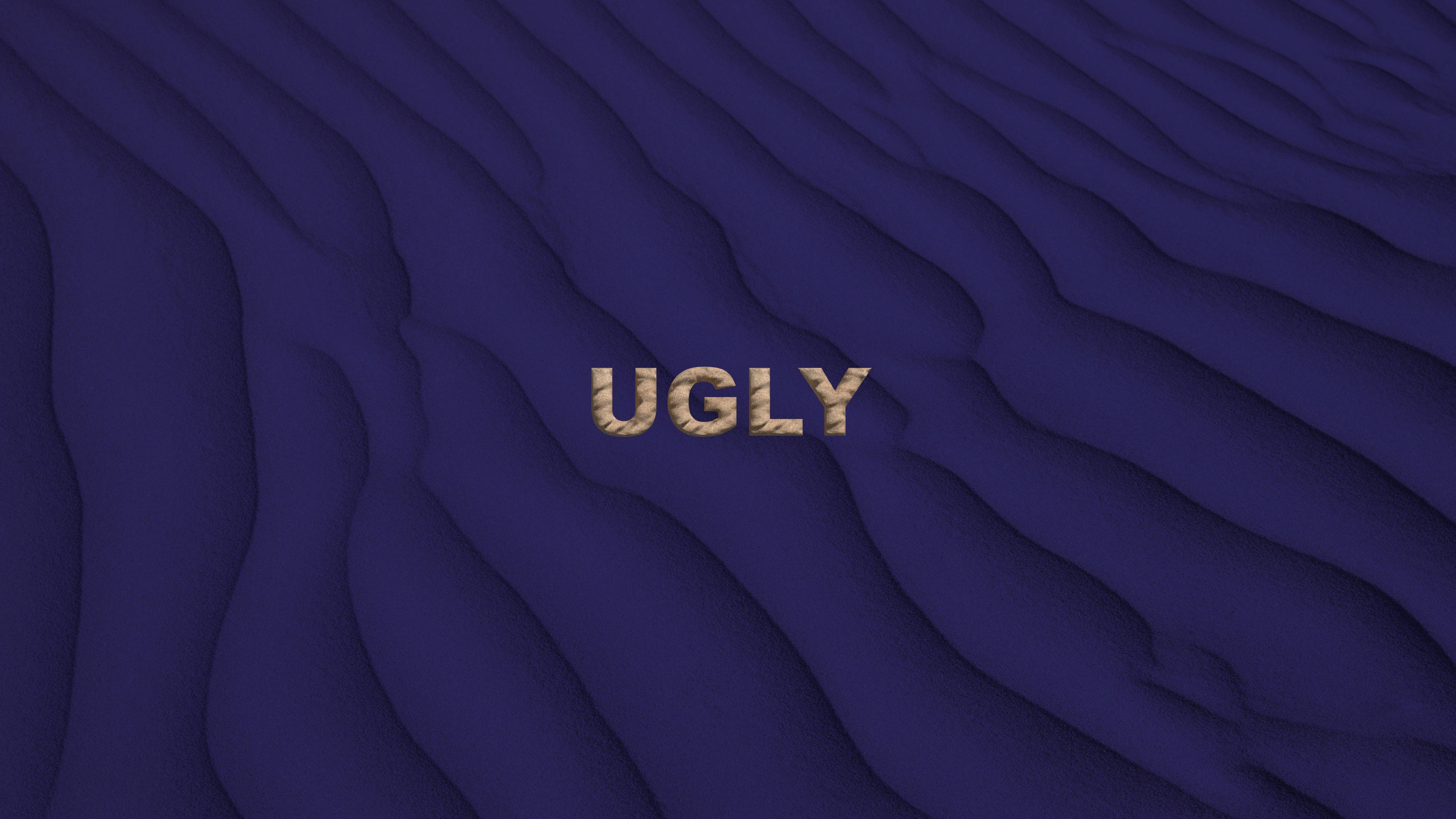 ugly 桌布 壁紙 — 「ugly」這個字以紋理金色字母呈現，放在深藍色波浪表面上，帶有柔和陰影。