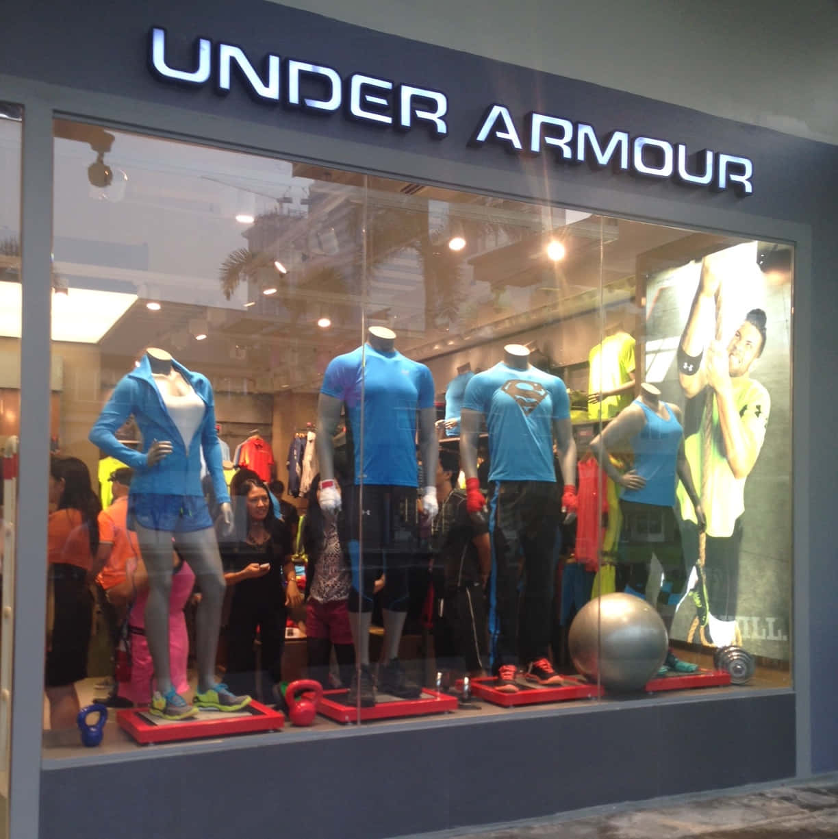 Under Armour 桌布 壁紙 — Under Armour 商店櫥窗展示，模特兒穿著運動服飾，配有健身器材，外面有購物者。