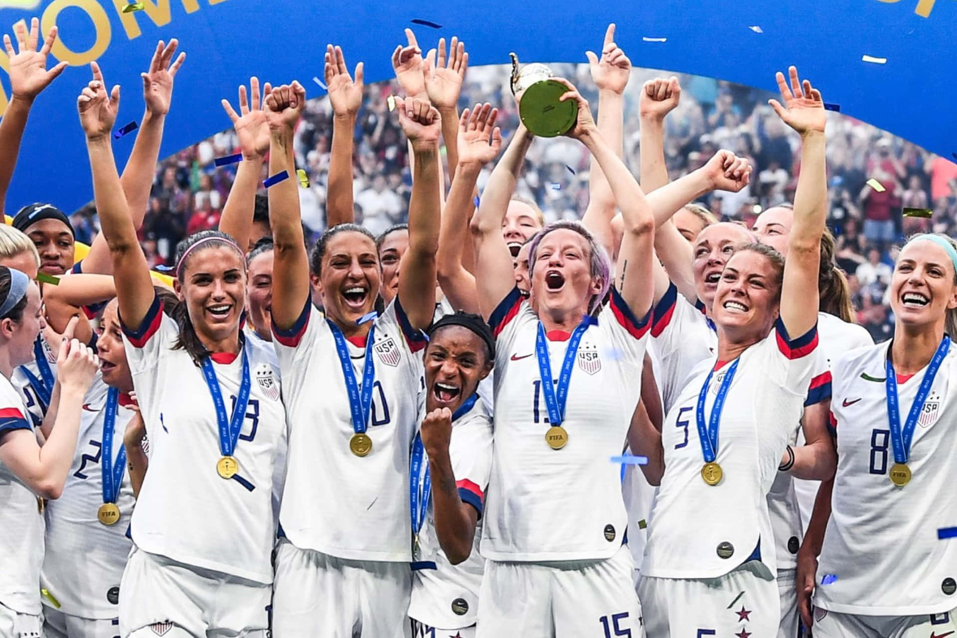  壁紙 — 美國女子足球隊在球場燈光下高舉獎盃和金牌慶祝勝利。