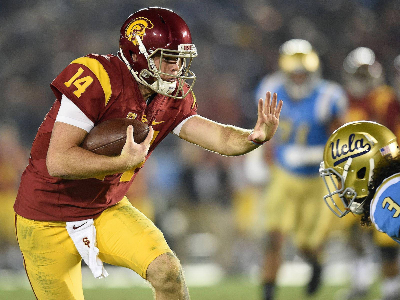 Football Players 桌布 壁紙 — USC 美式足球四分衛身穿栗色和金色制服，在對陣 UCLA 的夜間比賽中準備投球。