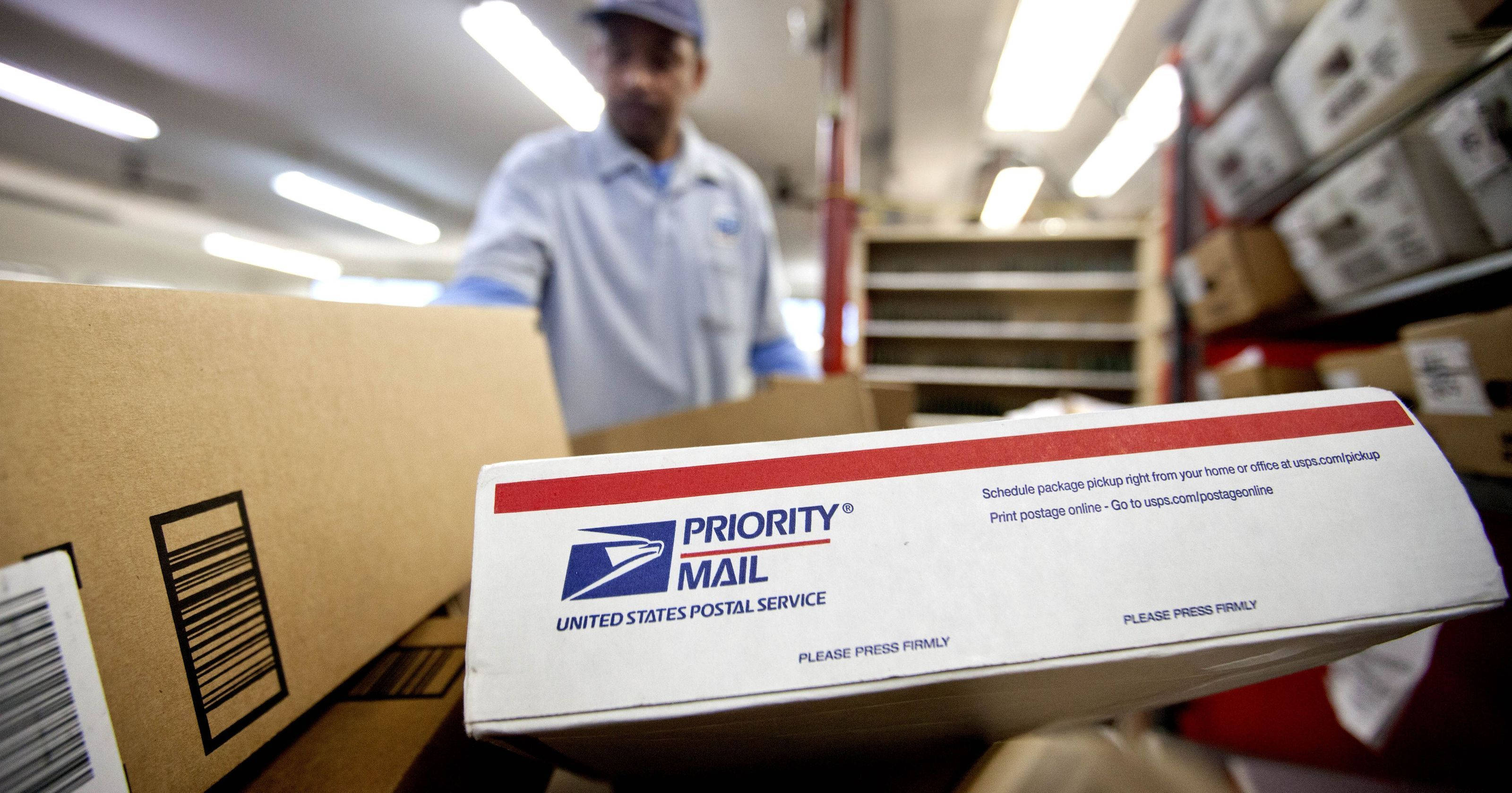Box 桌布 壁紙 — USPS設施內Priority Mail盒的特寫，背景有郵政工作人員模糊處理。