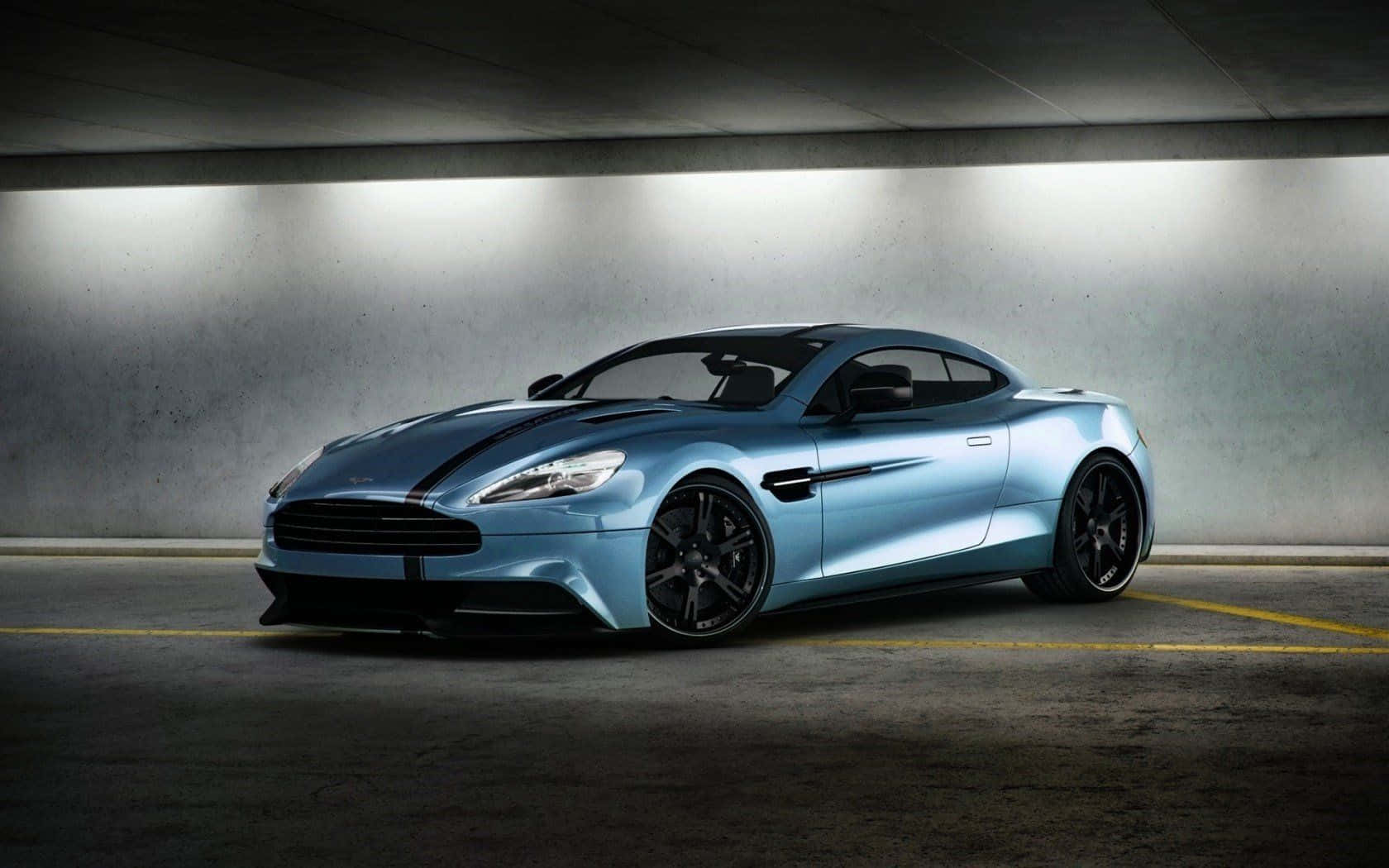 流暢奔馳的奧斯頓馬丁Vanquish 壁紙 — 一輛時尚的淺藍色 Aston Martin 跑車帶有黑色條紋，在混凝土地下停車場的明亮燈光下閃閃發光。