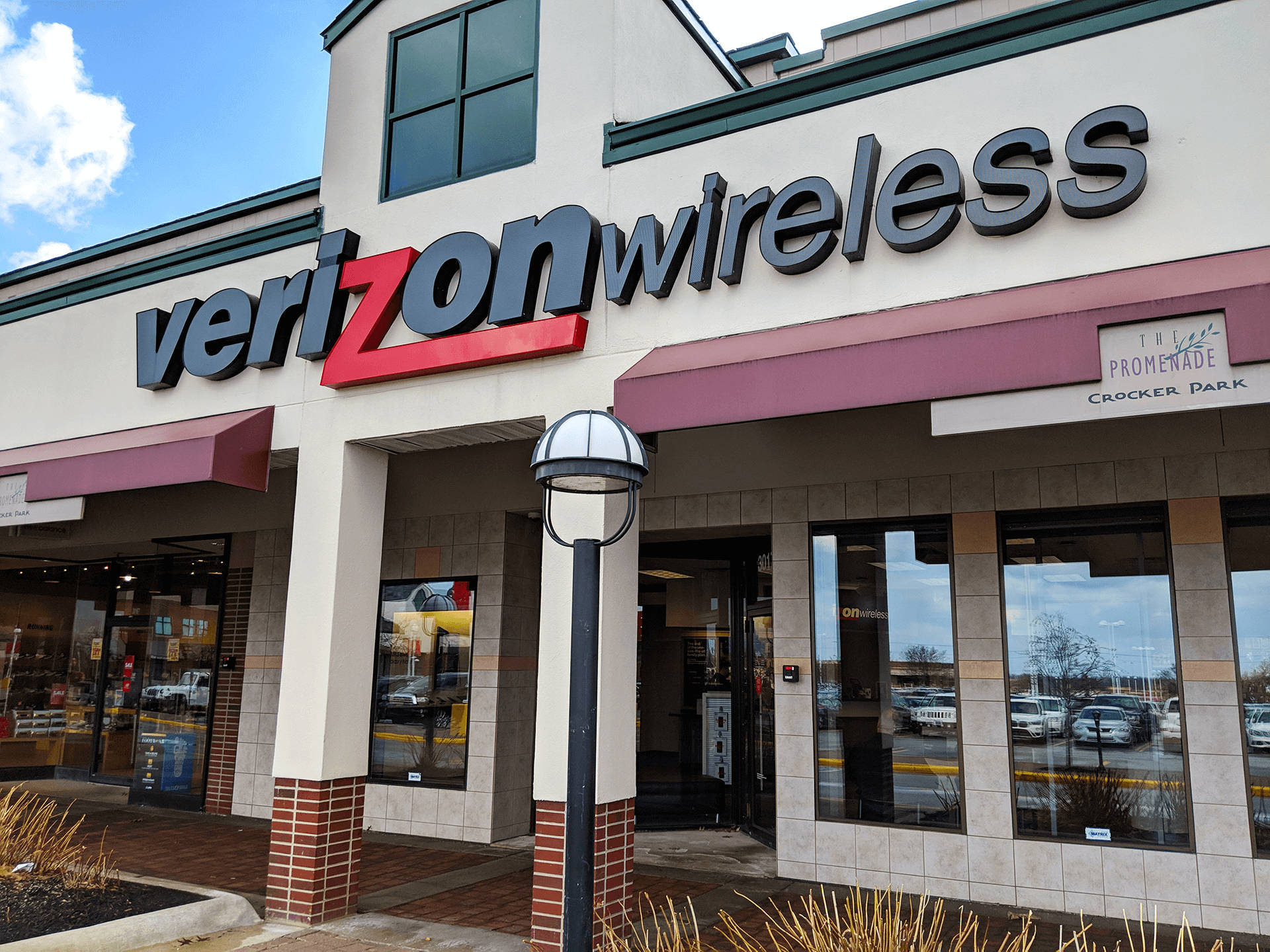 威訊 桌布 壁紙 — Verizon Wireless 店面外觀，在晴朗藍天和零星白雲下，設有醒目的紅色和灰色招牌。
