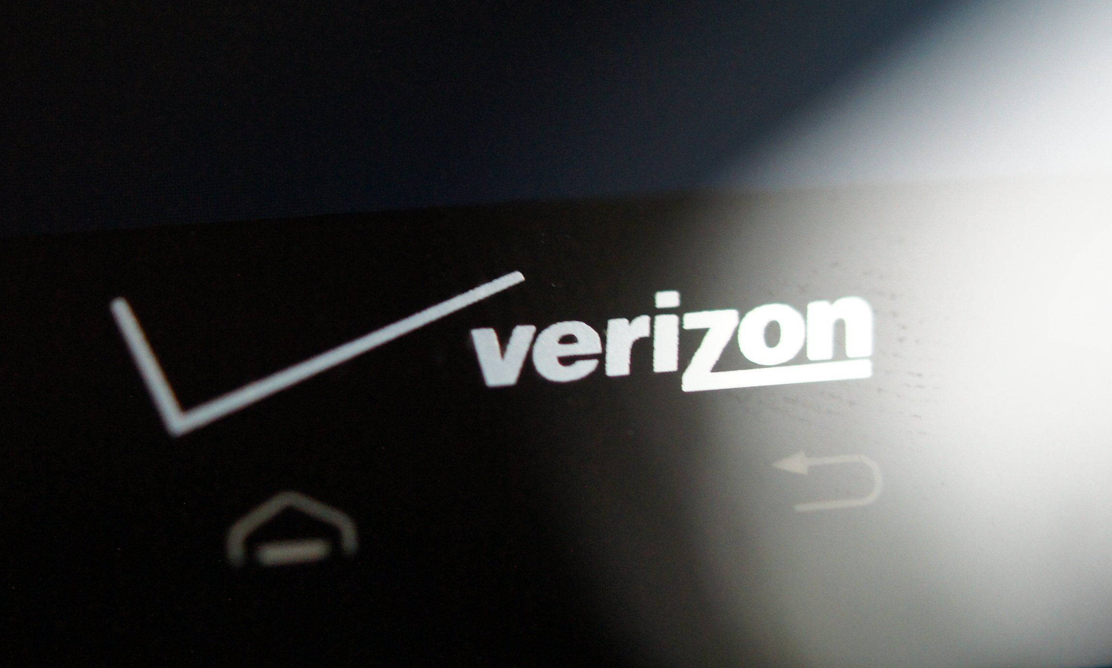 Verizon 桌布 壁紙 — Verizon 標誌在黑暗螢幕上以白色亮起，帶有模糊的導航圖示的特寫。