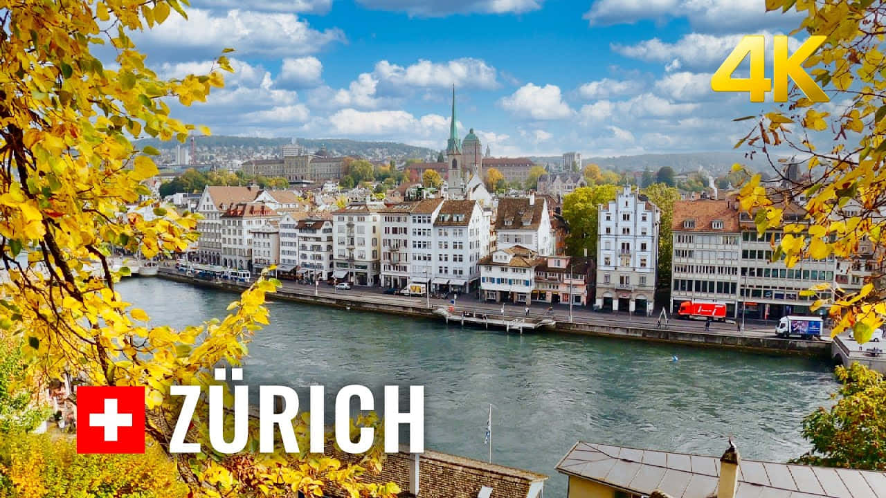 Zurich 桌布 壁紙 — 在明亮的藍天下，蘇黎世城市景觀的充滿活力的秋日景色，由河邊的金色樹葉框住。
