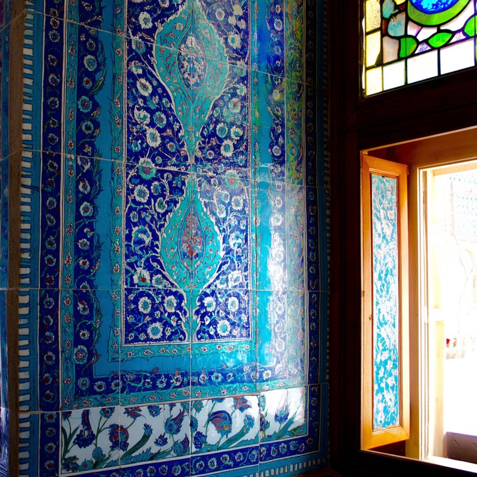 Blue Mosque Tile Detail 壁紙 — 充滿活力的藍色和藍綠色陶瓷瓷磚，帶有複雜的花卉和幾何圖案，裝飾在彩色玻璃窗旁邊的牆上。