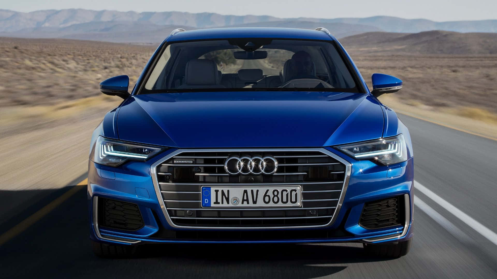 Audi A6 桌布 壁紙 — 一輛充滿活力的藍色奧迪轎車在沙漠公路上疾馳，周圍景物模糊，遠山在明亮的日光下清晰可見。