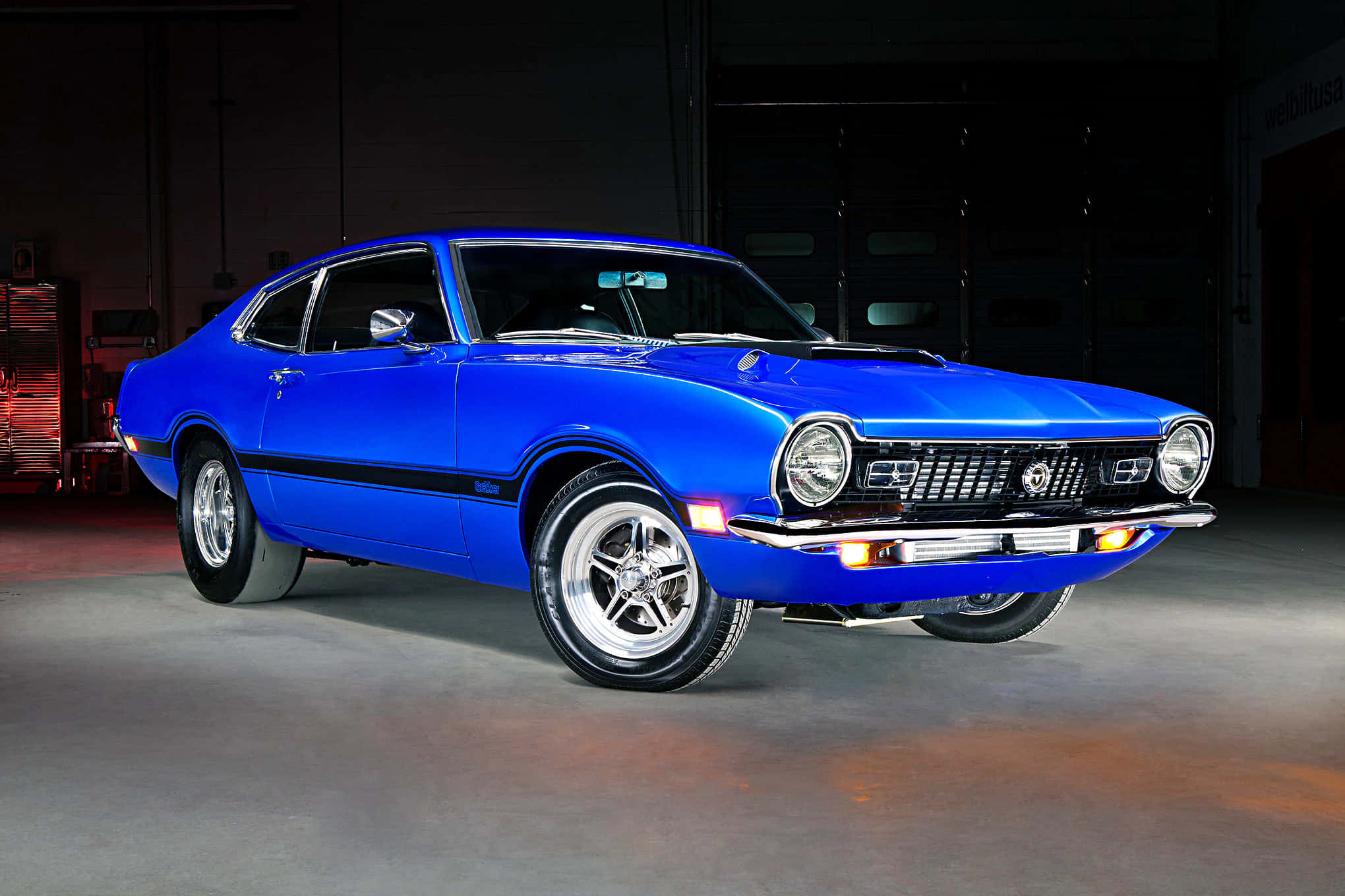 Ford Maverick 桌布 壁紙 — 一輛充滿活力的藍色經典肌肉車，帶有鍍鉻裝飾，在昏暗的工業車庫中於攝影棚燈光下閃閃發光。