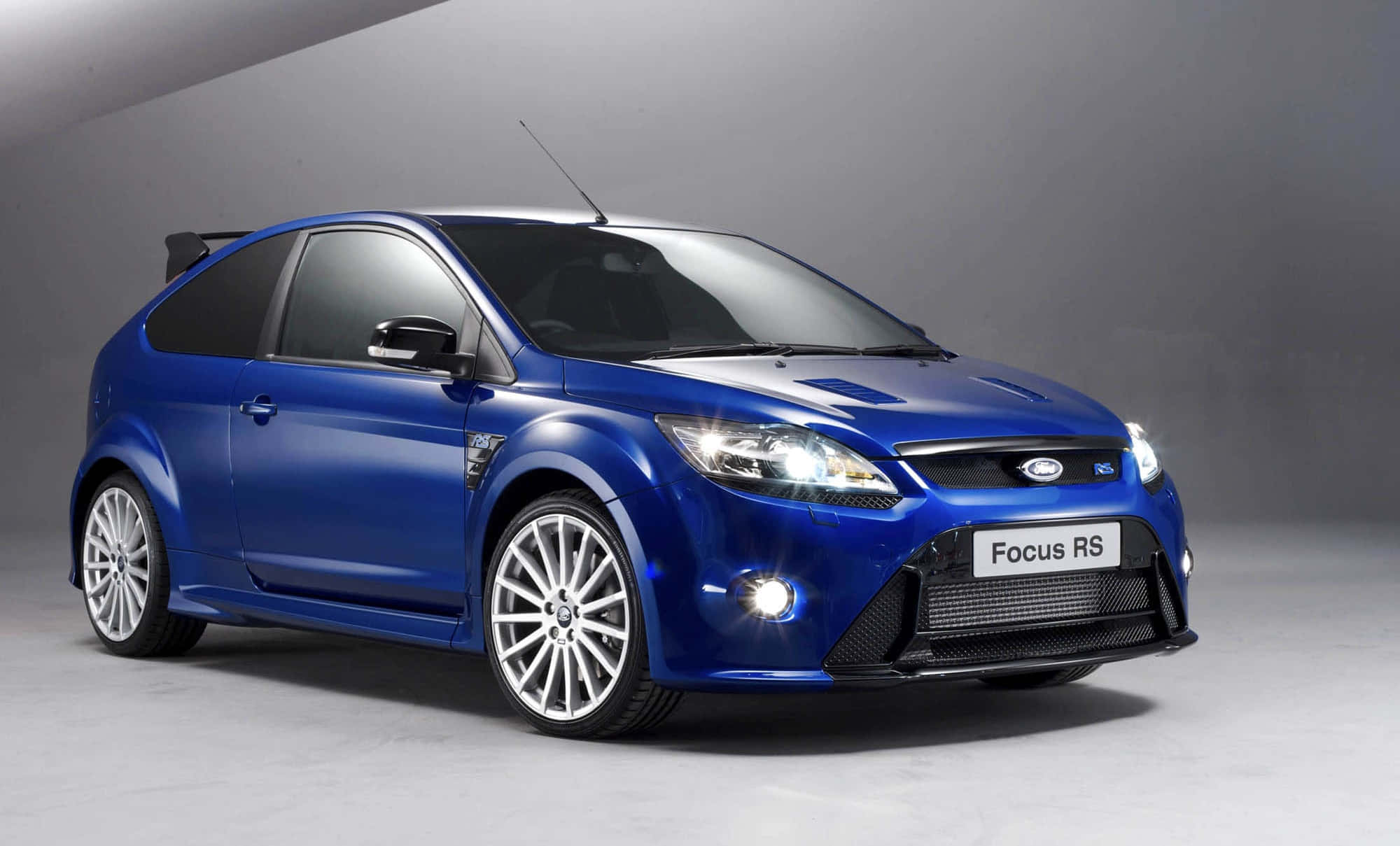 Ford Focus 桌布 壁紙 — 一輛充滿活力的藍色福特福克斯RS跑車在工作室燈光下閃耀，背景為極簡灰色。