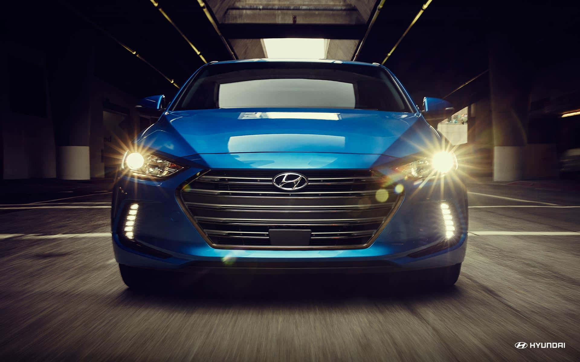 Hyundai Elantra 桌布 壁紙 — 一輛充滿活力的藍色現代汽車，帶著發光的車頭燈，在光線昏暗的城市隧道中疾馳前進。