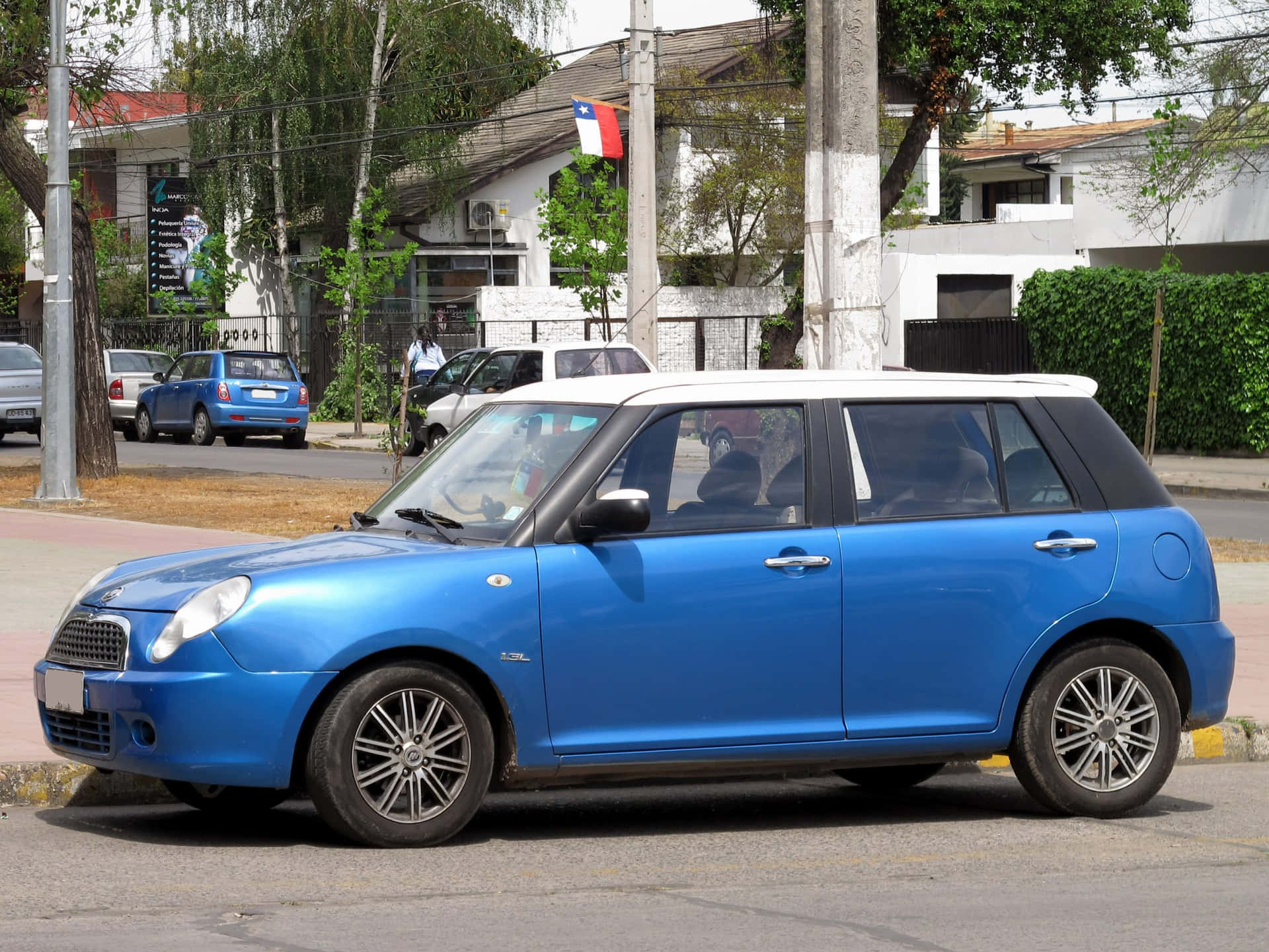  壁紙 — 一輛鮮藍色白色車頂的Mini Cooper停泊在陽光普照、兩旁種滿樹木和房屋的城市街道上。