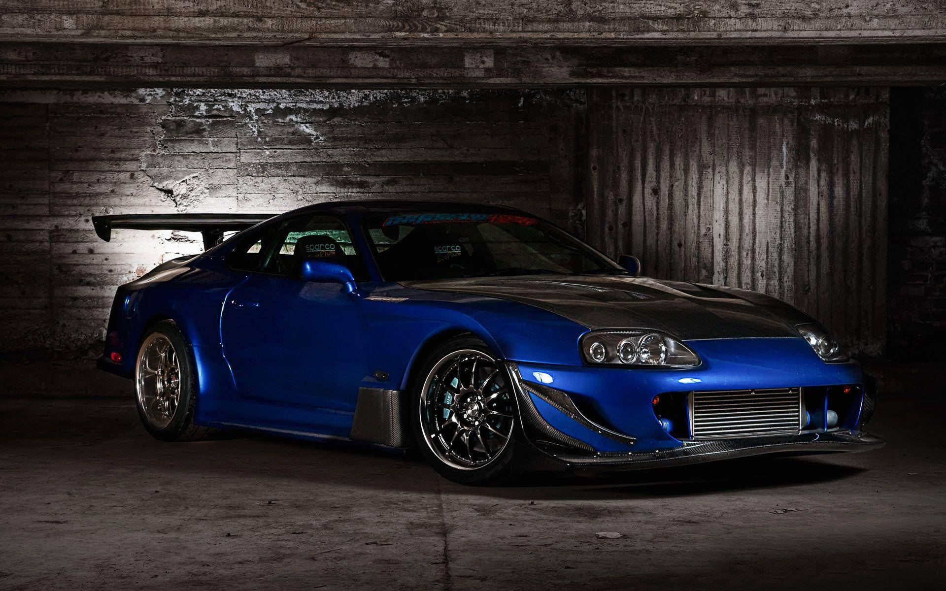 藍色改裝跑車在昏暗的混凝土車庫中，帶有聚光燈效果。 — Toyota Supra 壁紙