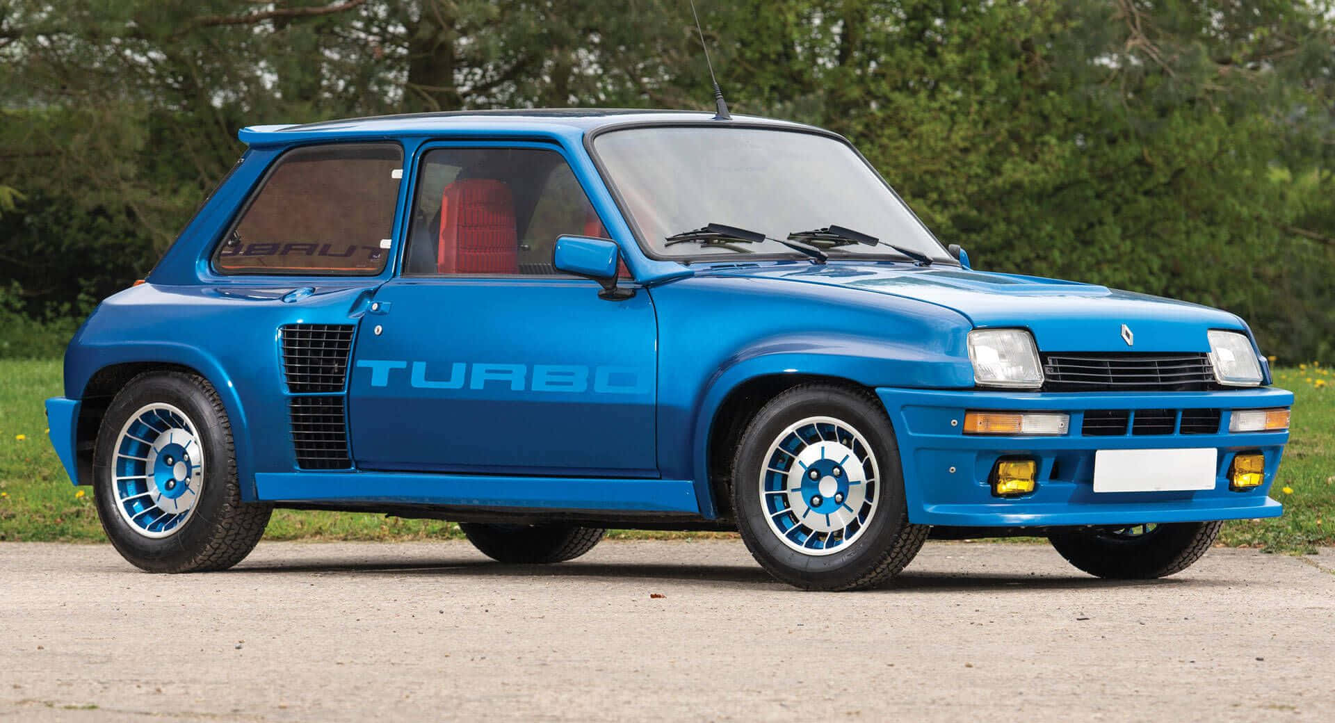 Renault 5 Turbo 桌布 壁紙 — 一輛充滿活力的藍色雷諾5 Turbo跑車停在碎石上，背景有綠樹。