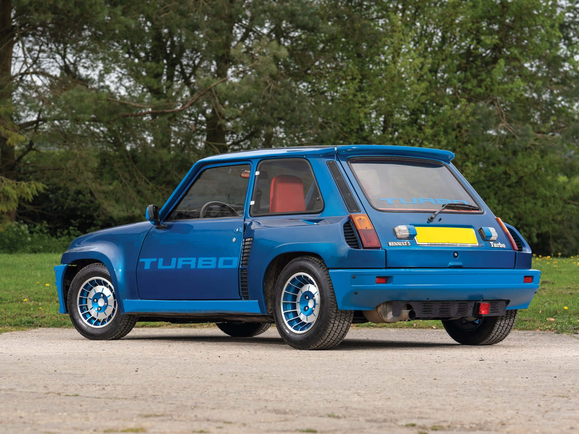 Renault 5 Turbo 桌布 壁紙 — 一輛充滿活力的藍色雷諾5 Turbo跑車停在碎石上，背景有綠樹。