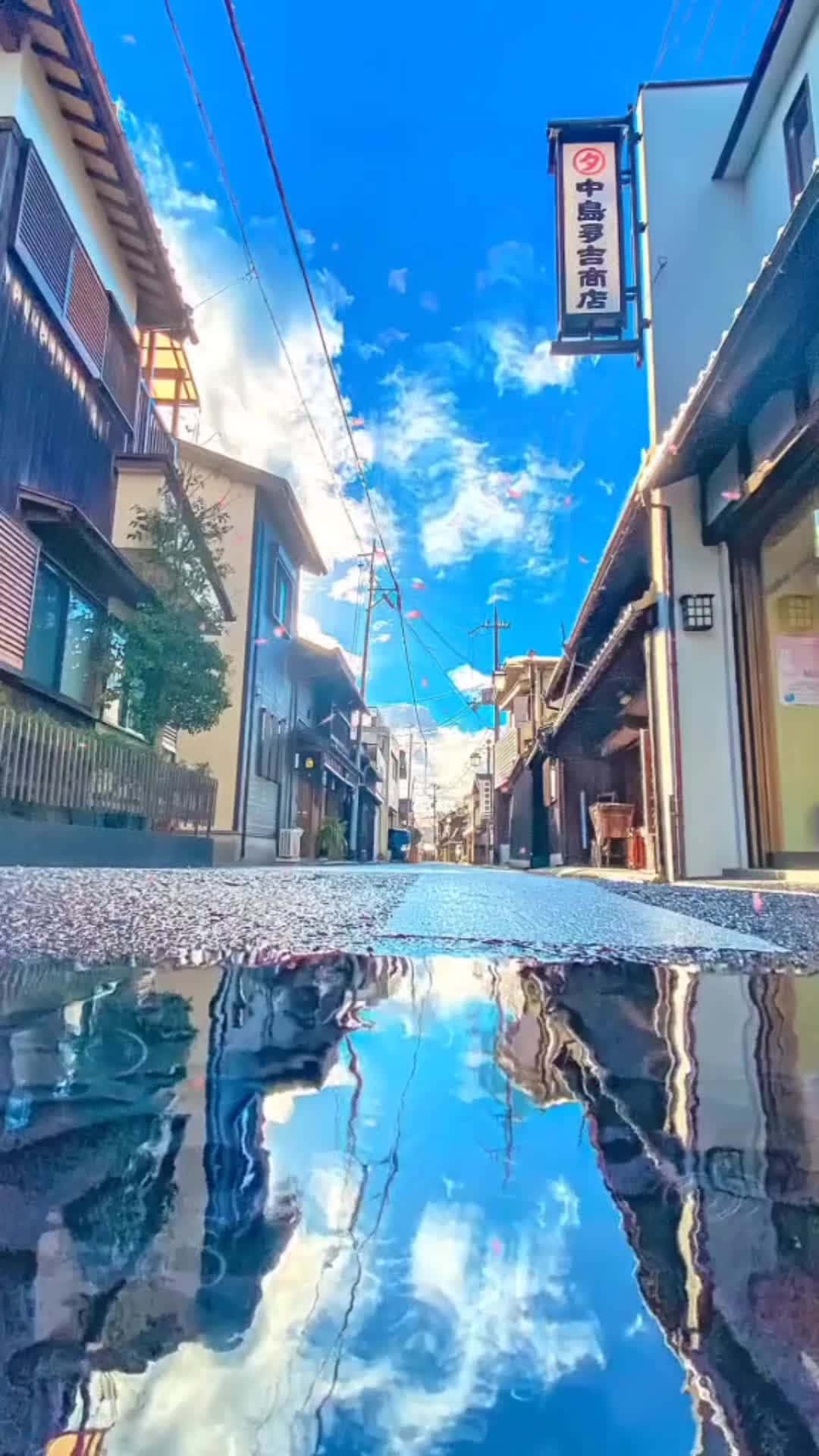  壁紙 — 充滿活力的藍天和蓬鬆的雲朵倒映在狹窄的傳統日本街道上的水坑中，街道兩旁是木製建築。