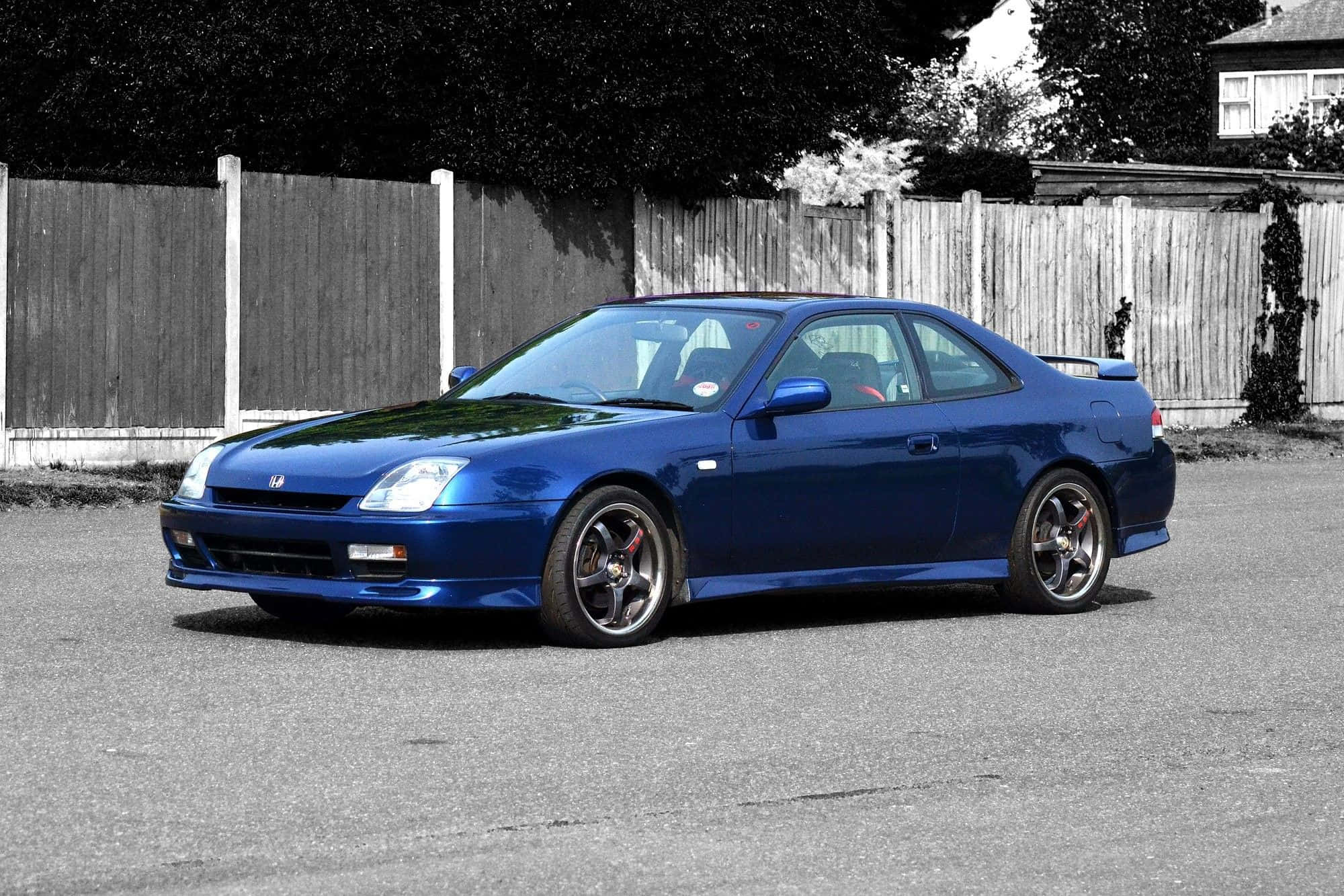 Honda Prelude 桌布 壁紙 — 一輛充滿活力的藍色跑車停在柏油路上，背景有黑白圍欄和樹木。