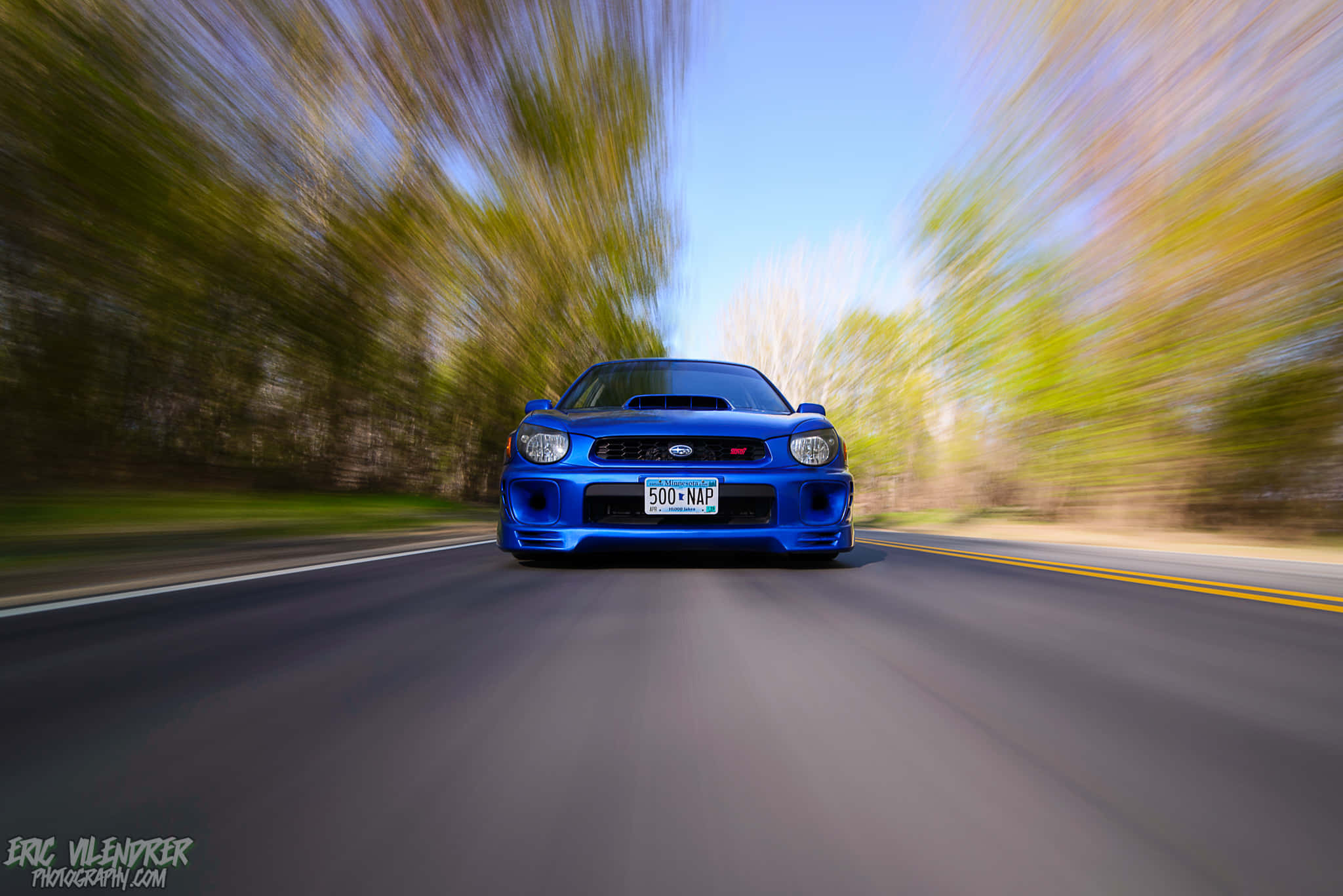 Subaru Impreza 桌布 壁紙 — 一輛充滿活力的藍色跑車在樹木成蔭的道路上疾馳，背景帶有動態模糊效果。