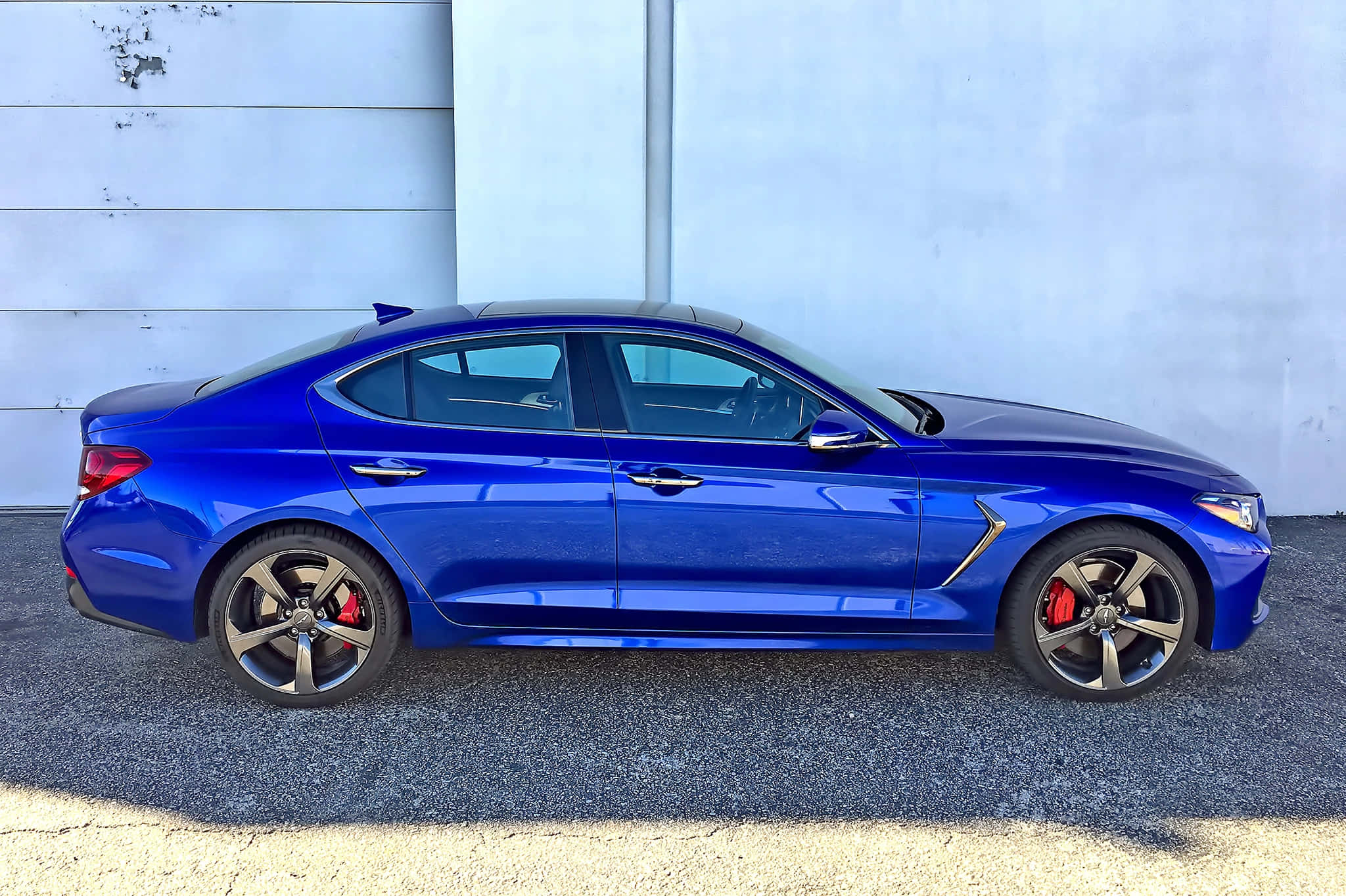 Genesis G70 桌布 壁紙 — 一輛充滿活力的藍色運動轎車，帶有紅色制動卡鉗，停在礫石上，背景是淺灰色牆壁。