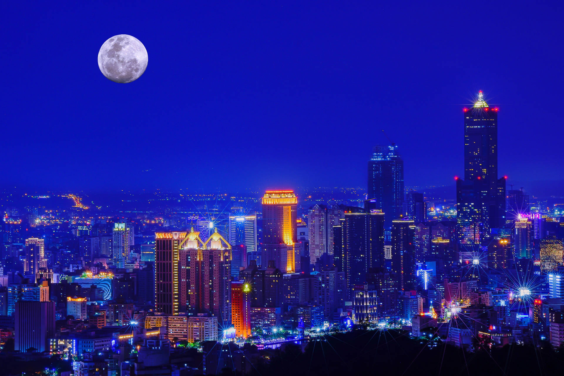 夜晚發光的城市景觀，高樓大廈和上方的滿月。 — 台灣 壁紙
