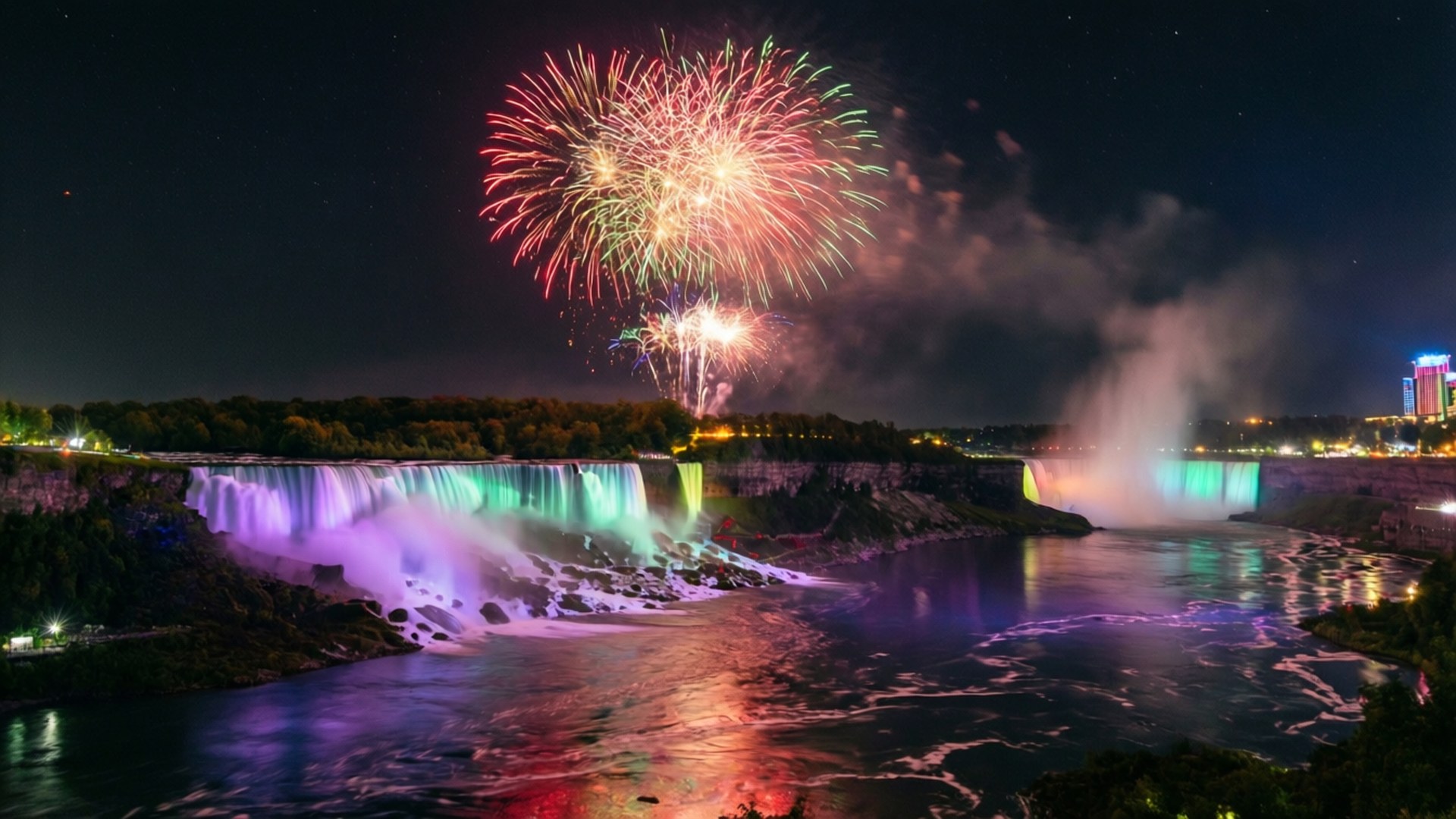 Fireworks Over Niagara 壁紙 — 色彩繽紛的煙火在夜晚照亮尼亞加拉大瀑布的上方爆炸，在下方霧氣瀰漫的河流上投下多彩的倒影。