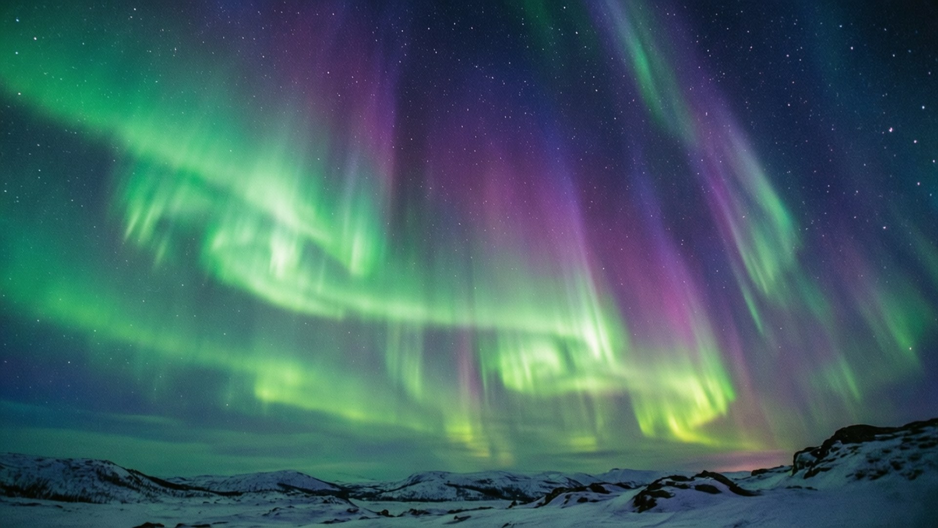 Aurora Over Snow 壁紙 — 鮮豔的綠色和紫色極光在雪覆蓋的山脈上方的星空夜空中舞動。