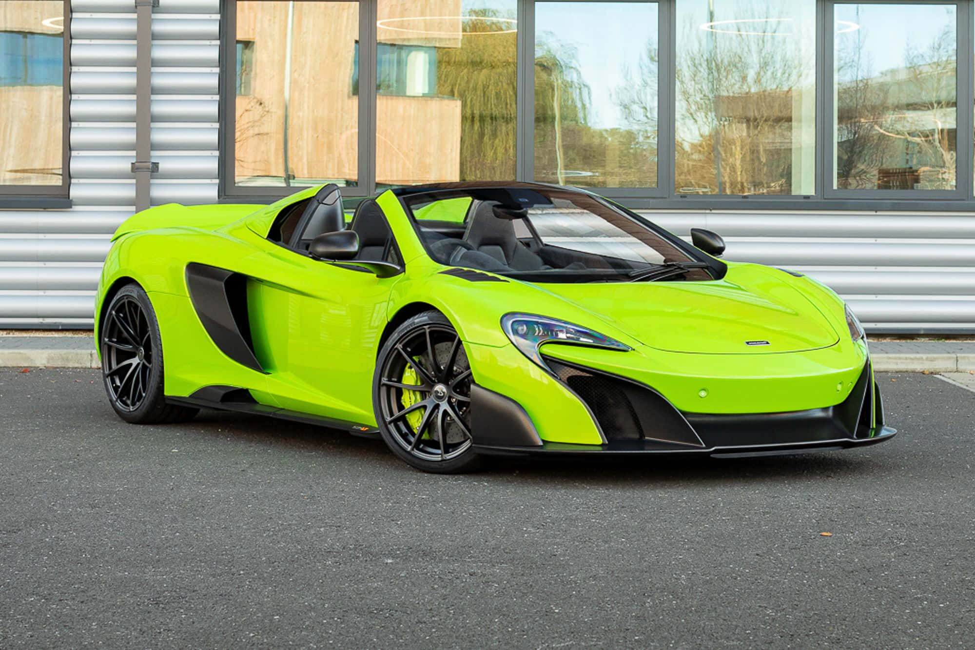 Mclaren 675lt Spider 桌布 壁紙 — 一輛鮮豔的青檸綠色McLaren 570S Spider停放在瀝青路面上，前方是帶有反光窗戶的現代建築。