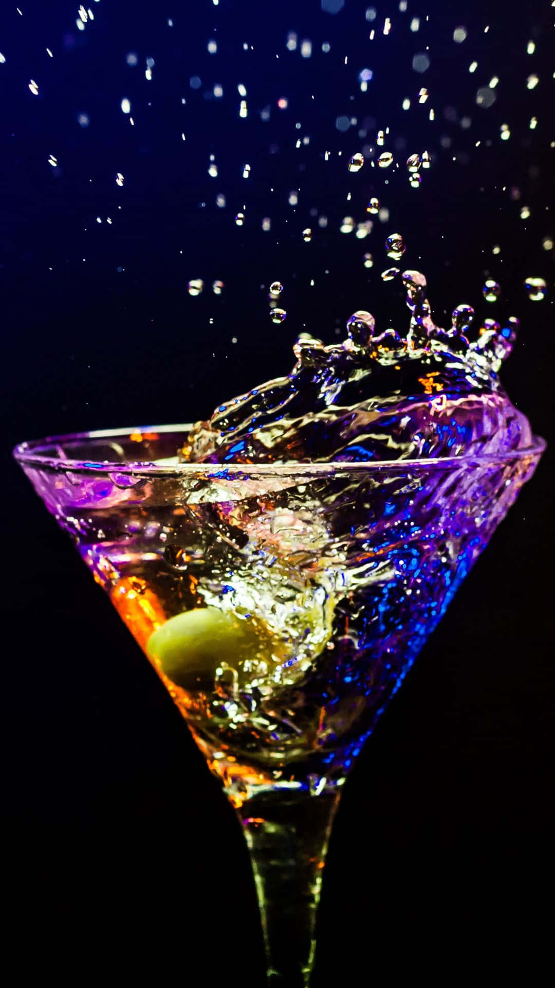  壁紙 — 一個充滿活力的馬丁尼杯，內有綠色橄欖，在深色背景下濺起彩虹色的液體。