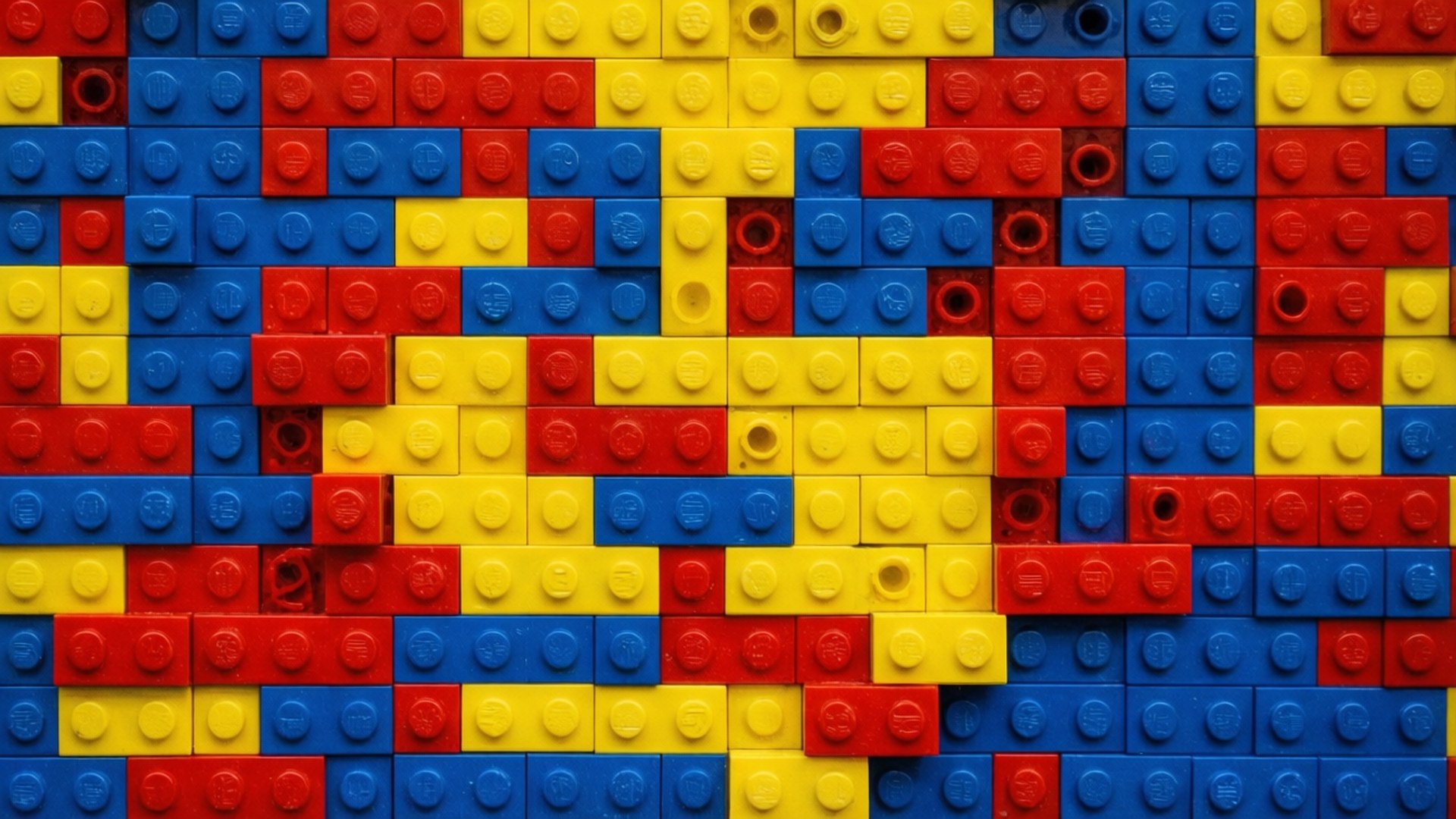 Vibrant Lego Brick Pattern 壁紙 — 由紅色、黃色和藍色LEGO積木組成的充滿活力的馬賽克，形成帶有可見凸點和間隙的紋理抽象圖案。