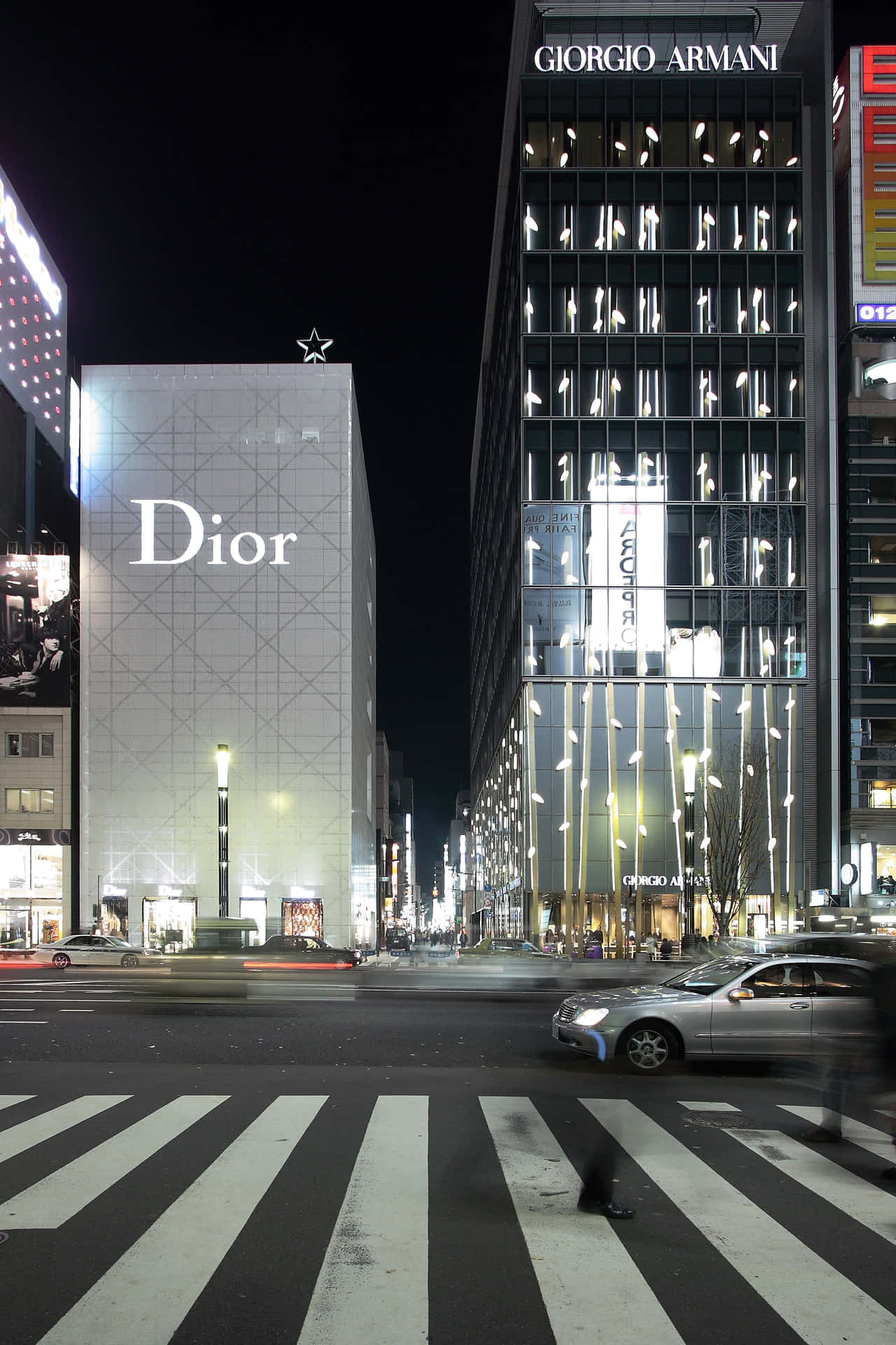  壁紙 — 充滿活力的夜景城市景觀， featuring 亮燈的 Dior 和 Giorgio Armani 建築物，繁忙街道上汽車燈光形成光軌。