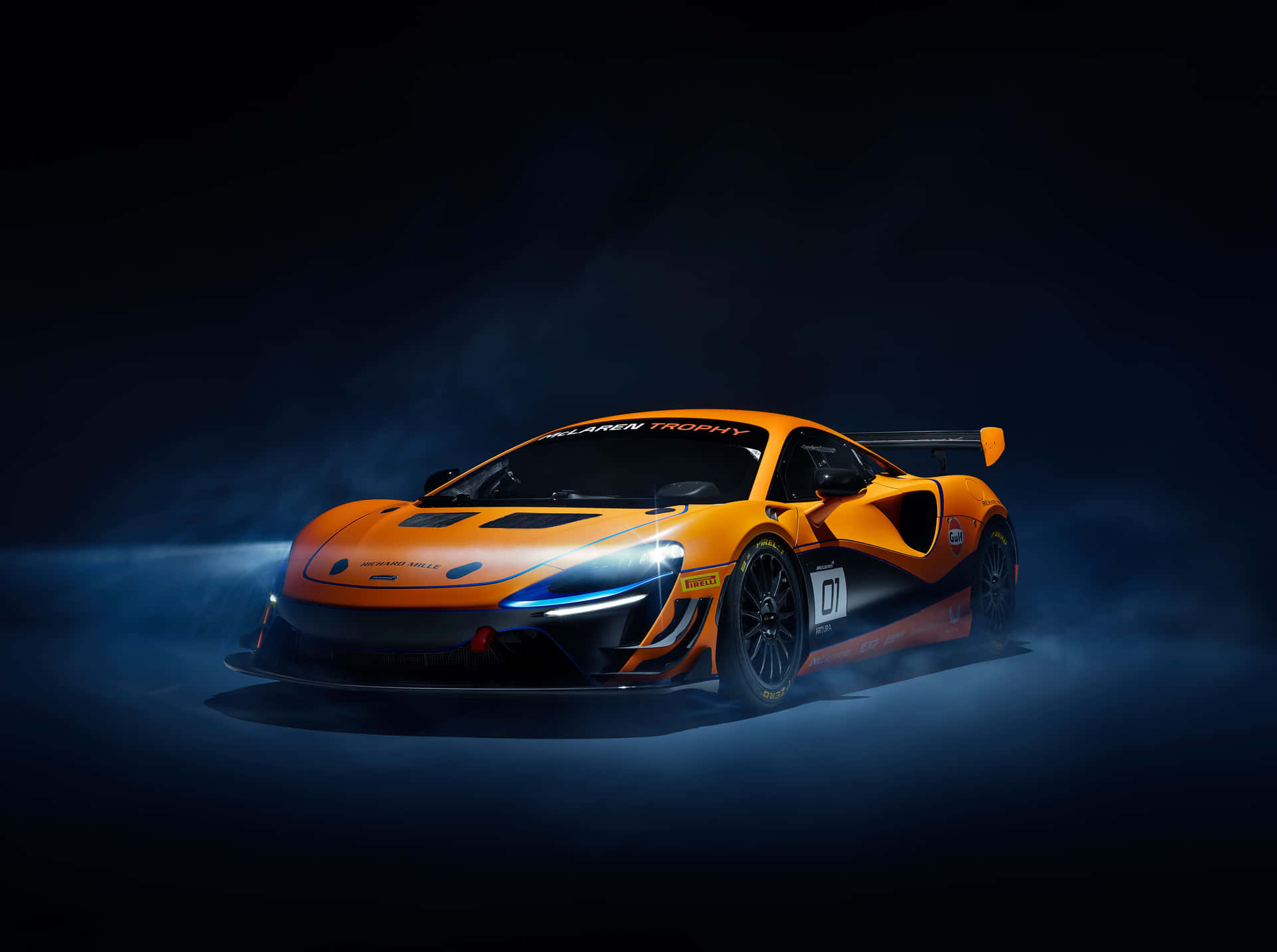  壁紙 — 一輛充滿活力的橙色McLaren賽車，在黑暗的攝影棚環境中，車頭燈發光並揚起藍色煙霧。