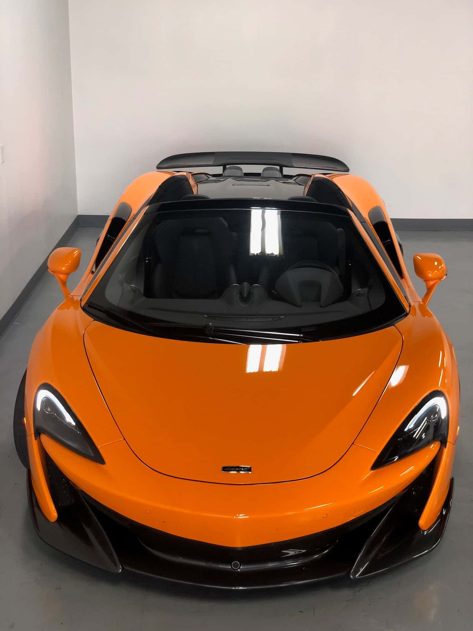 Mclaren 600lt Spider 桌布 壁紙 — 一輛充滿活力的橙色McLaren跑車，配備黑色車頂和時尚的空氣動力學設計，在明亮的燈光下停放在室內。