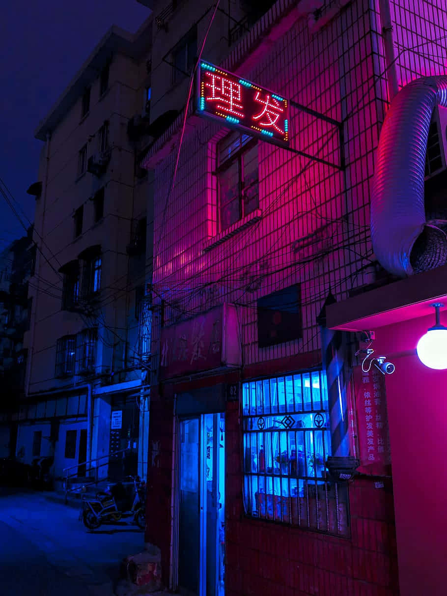 Red Light District 桌布 壁紙 — 鮮豔的粉紅色和藍色霓虹燈照亮了夜晚一條骯髒的城市小巷，在風化的建築物和一輛停放的摩托車上投射出超現實的光芒。