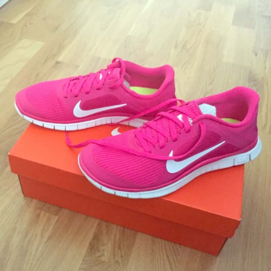 Pink Shoes 桌布 壁紙 — 鮮豔的粉紅色Nike跑鞋，帶有白色swoosh標誌，放在明亮的橙色盒子上，置於淺色木地板上。