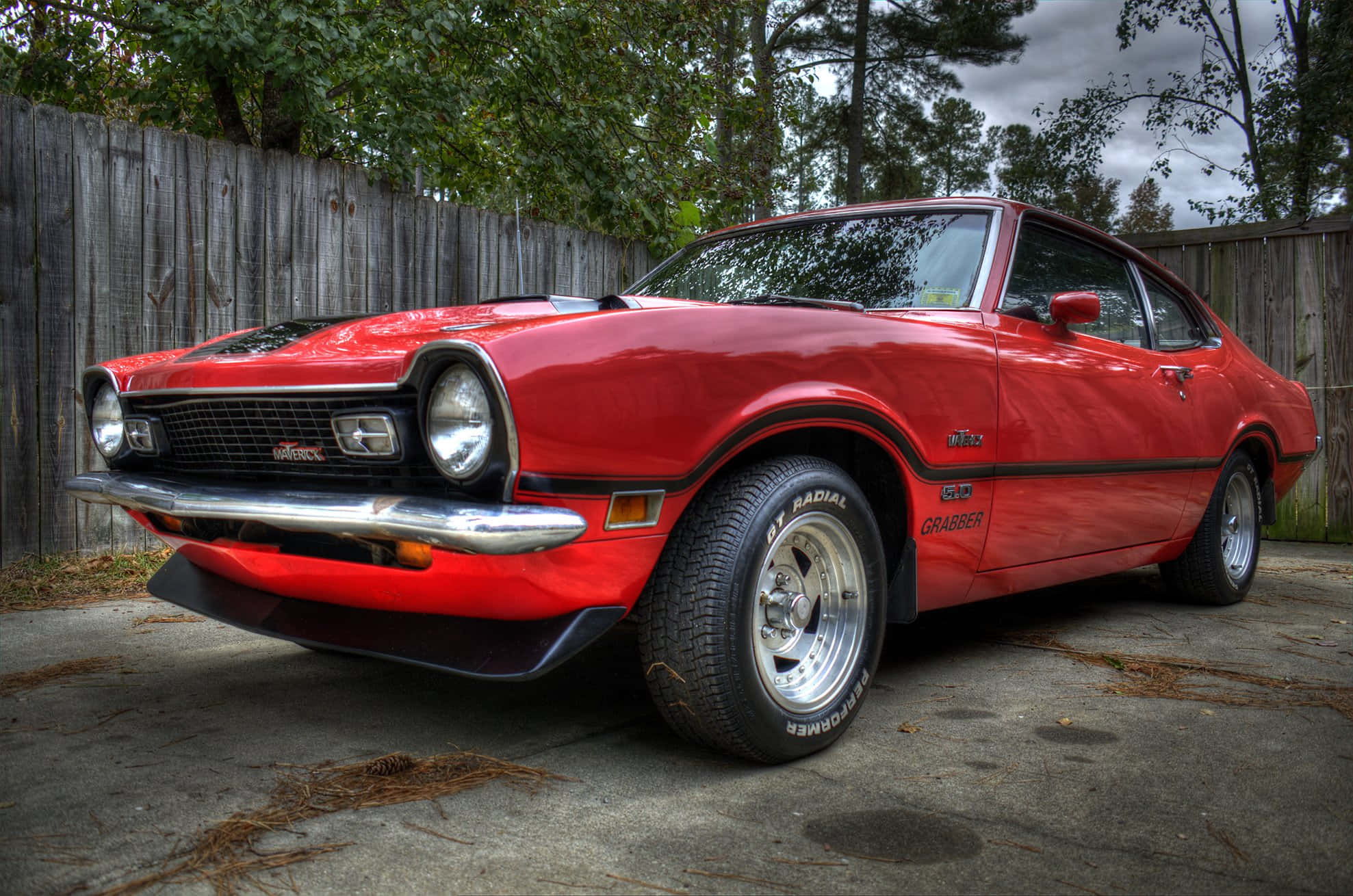 Ford Maverick 桌布 壁紙 — 一輛充滿活力的紅色經典肌肉車，帶有鍍鉻裝飾和子午線輪胎，停在混凝土車道上，旁邊是風化的木柵欄，天空多雲。