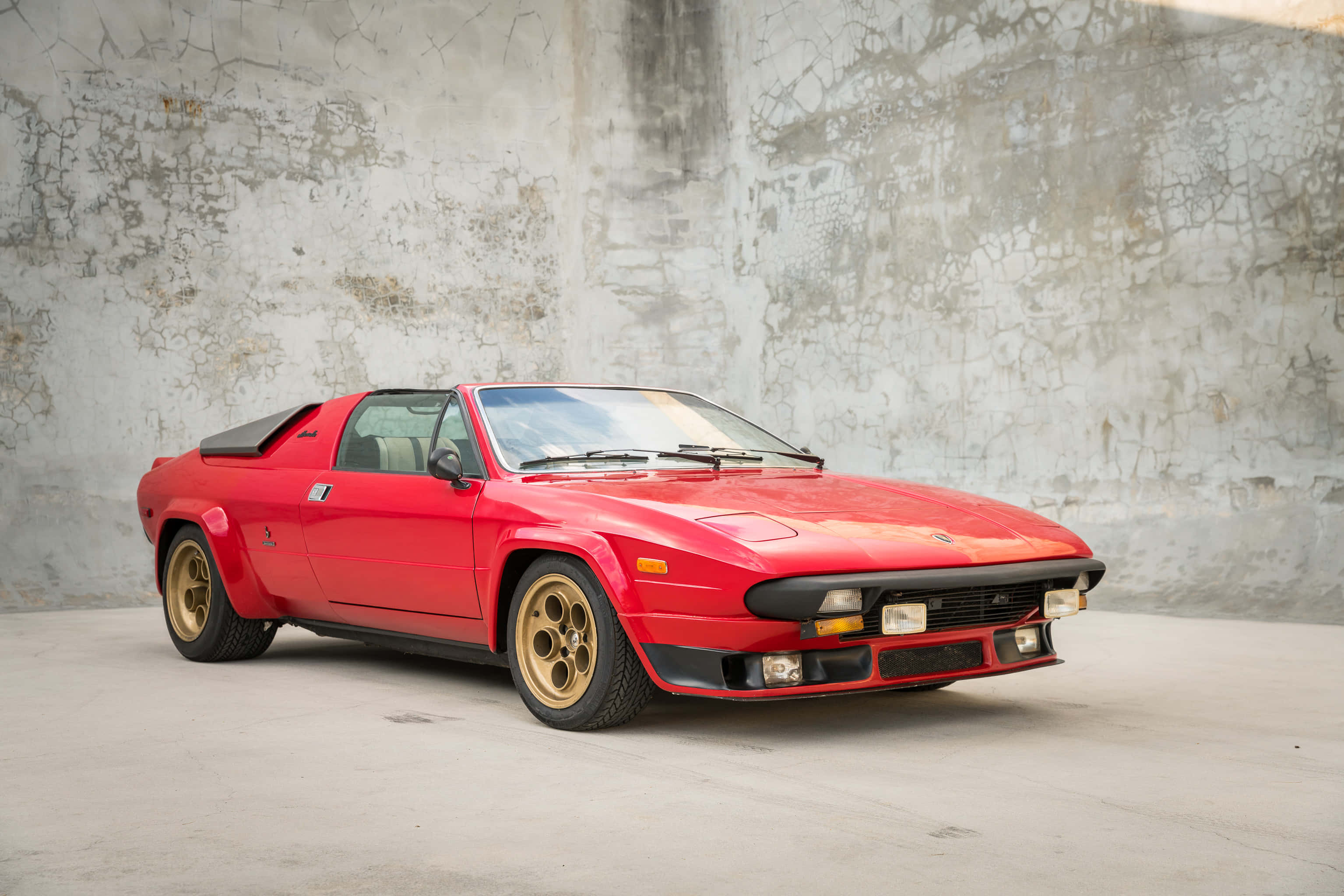 Lamborghini Silhouette 桌布 壁紙 — 一輛鮮紅色經典跑車配金色輪胎，停泊在風化混凝土牆前。