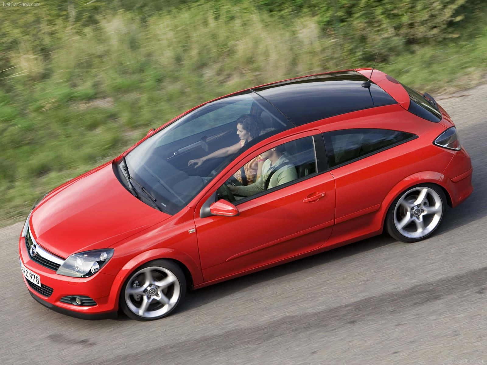 Opel Astra 桌布 壁紙 — 一輛充滿活力的紅色轎跑車沿著蜿蜒的道路疾馳，車內有兩個人，綠意隨著移動變得模糊。