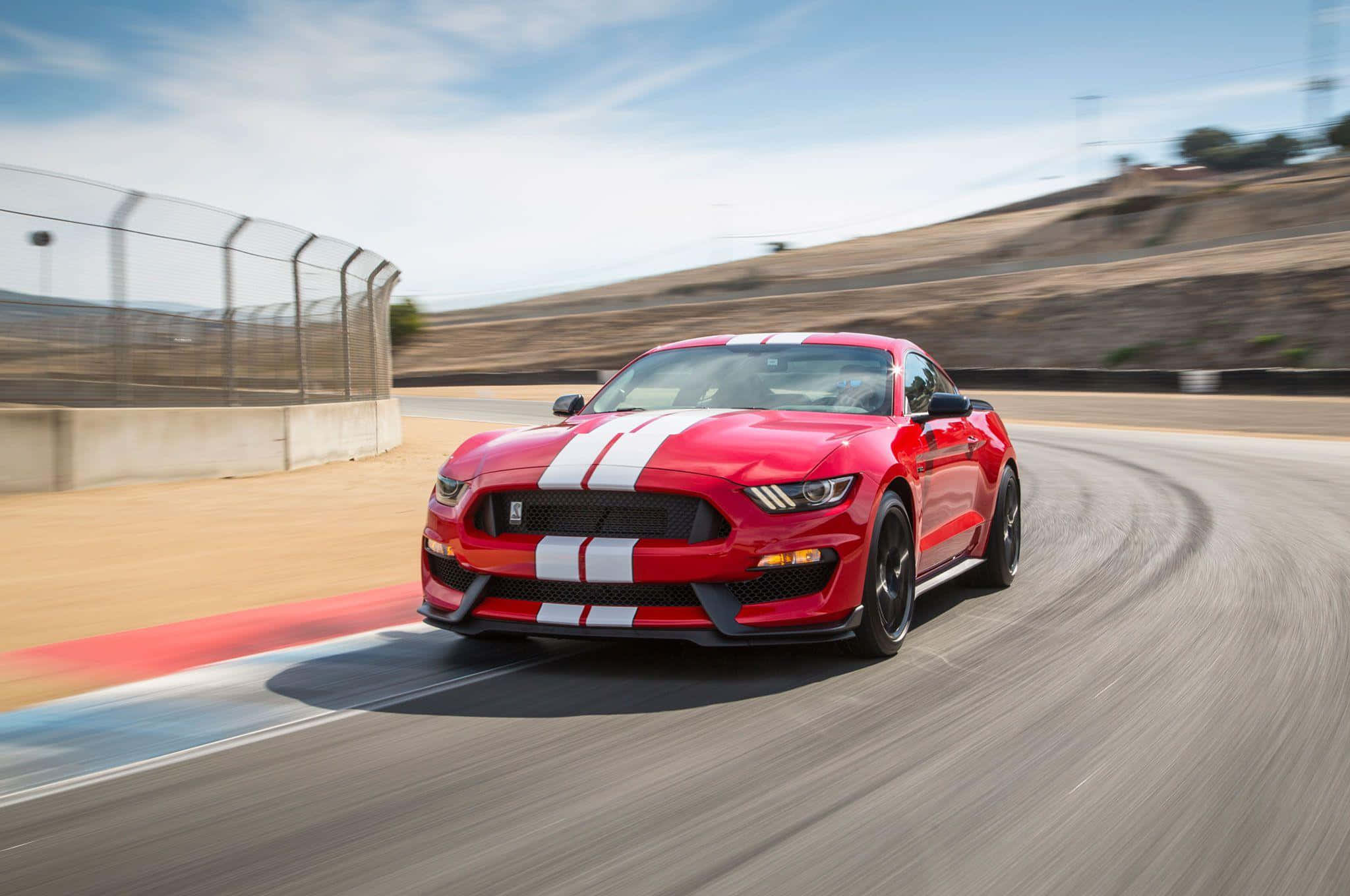Ford Mustang Shelby Gt350 桌布 壁紙 — 一輛帶有白色賽車條紋的鮮紅色福特野馬在陽光明媚的賽道彎道上飛馳。