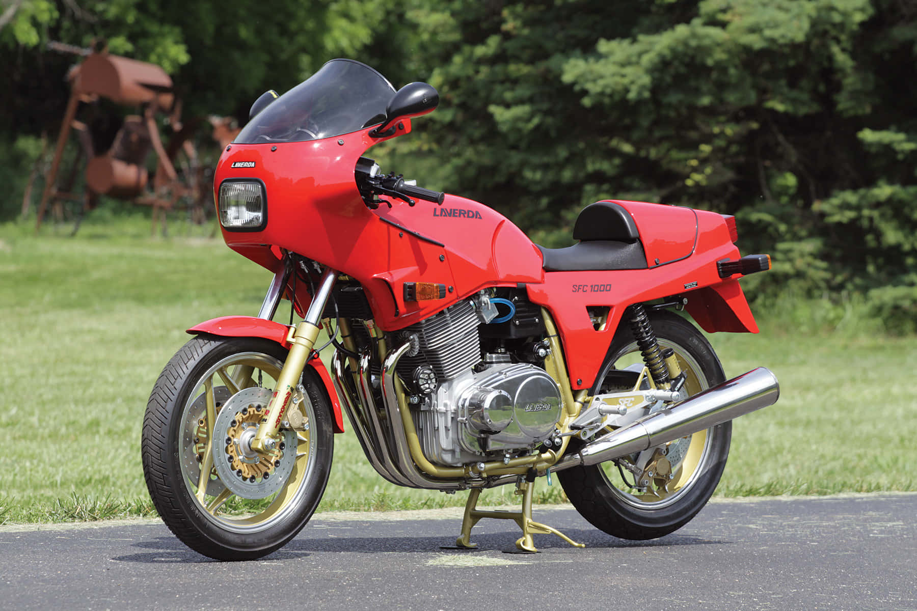  壁紙 — 一輛鮮紅色的Laverda SFC 1000摩托車，配備金色前叉和鍍鉻裝飾，停在鋪砌的道路旁，旁邊是茂盛的綠色草坪。