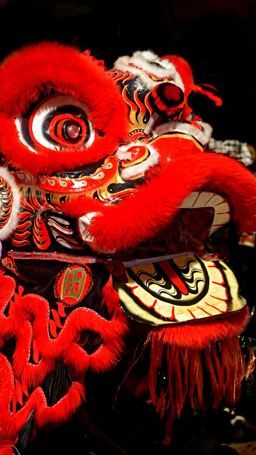  壁紙 — 一件鮮紅色的舞獅服裝，帶有複雜的黑色和金色圖案，在戲劇性的舞台燈光下閃耀。