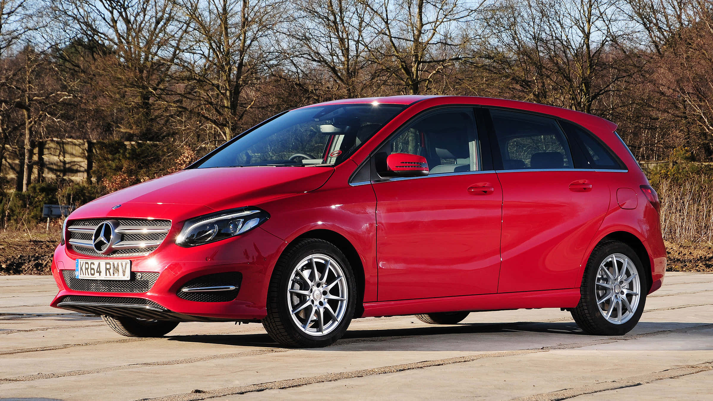 Mercedes Benz B-class 桌布 壁紙 — 一輛鮮紅色的Mercedes-Benz B-Class掀背車停放在鋪砌的停車場，背景有光禿禿的樹木，在晴朗的日光下。