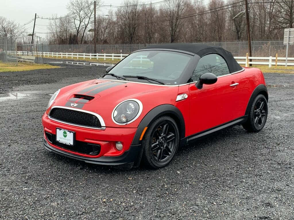  壁紙 — 一輛鮮紅色MINI Cooper敞篷車，帶有黑色飾邊，停放在碎石地上，天空多雲。