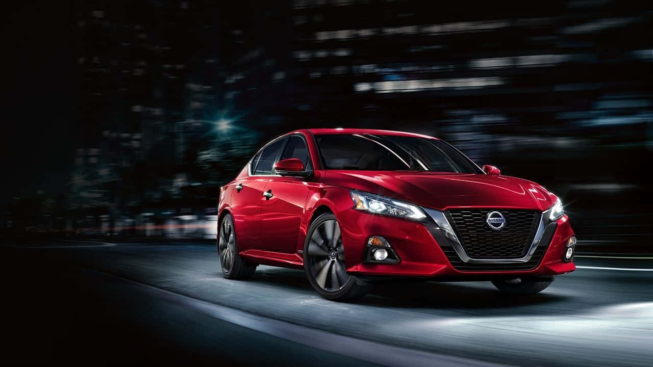 Nissan Altima 桌布 壁紙 — 一輛充滿活力的紅色轎車在模糊的夜間城市景觀中疾馳，閃爍的車頭燈劃破黑暗。