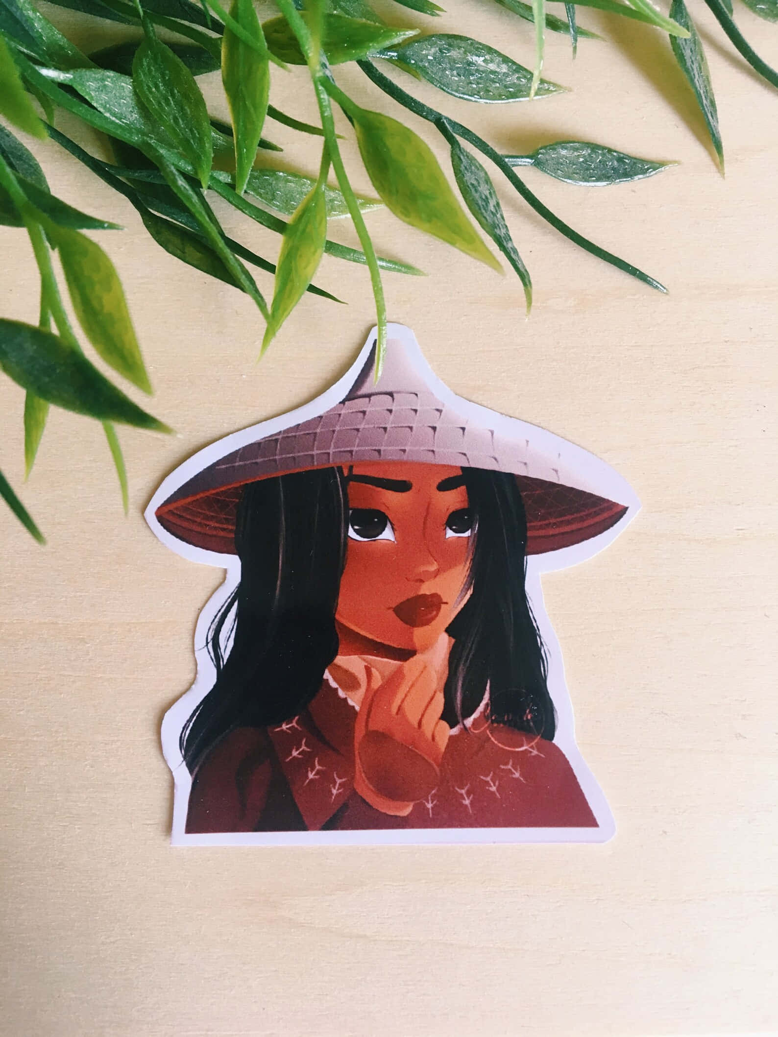 Raya 桌布 壁紙 — 一個充滿活力的貼紙，上面有一位戴著傳統圓錐形帽子的女士，放在木質表面上，旁邊是茂密的綠色樹葉。