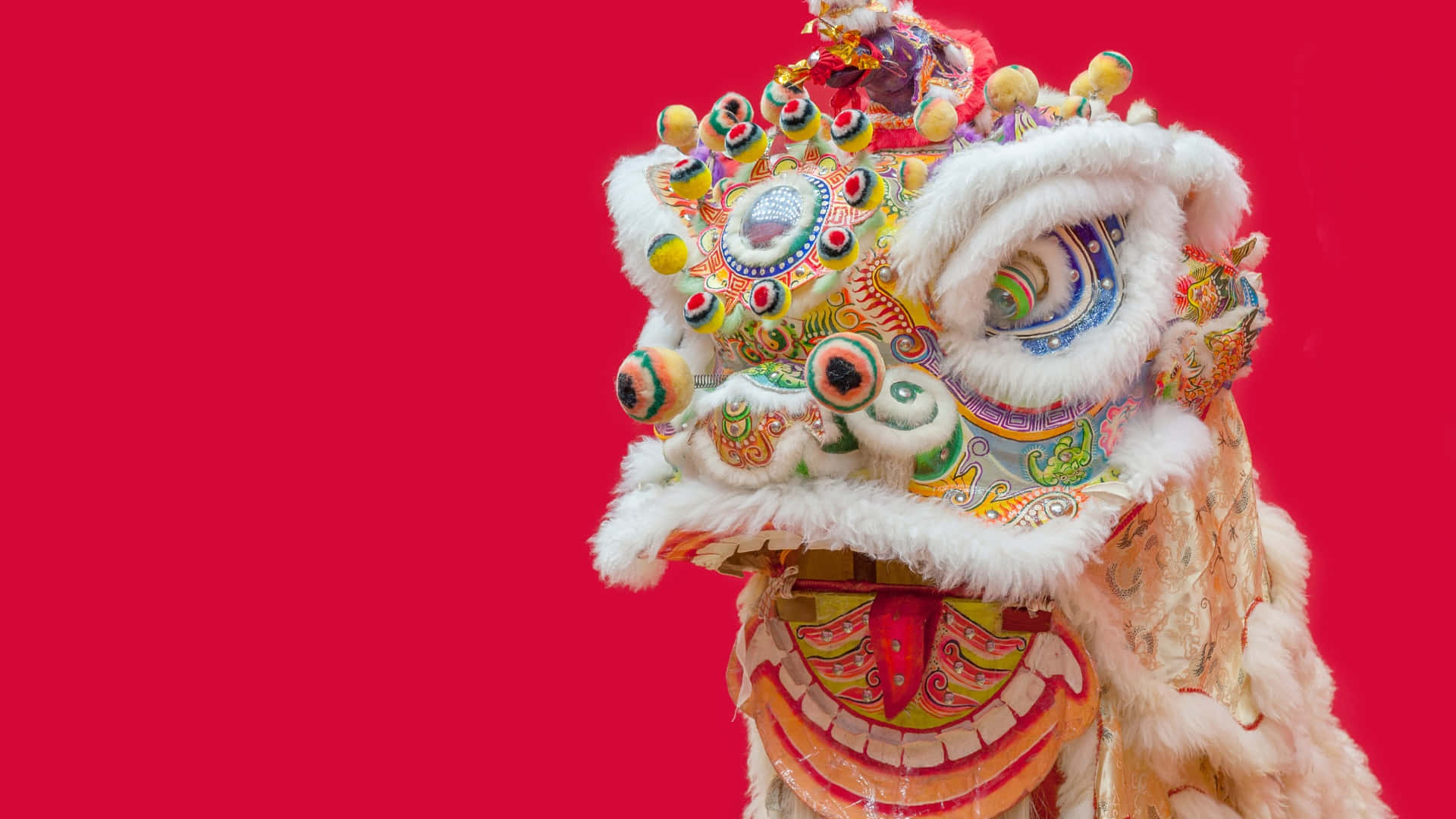  壁紙 — 鮮豔的傳統中國舞獅服裝，帶有複雜圖案和蓬鬆白色飾邊，背景為大膽的紅色。
